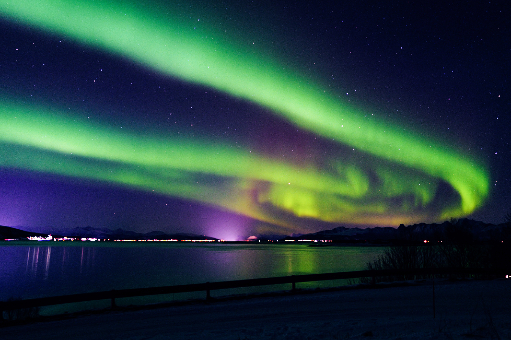 Aurora borealis over a calm lake and mountains at night, landscape photography by Leon Eule.