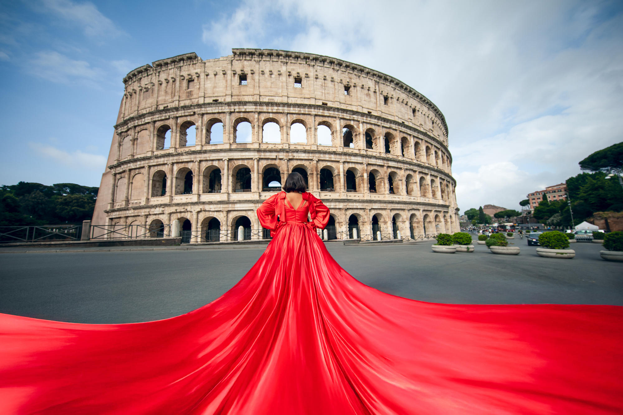 Olena Leliuk fashion photography in Rome featuring a woman in a flowing red dress in front of the Colosseum, showcasing cinematic style and creative composition