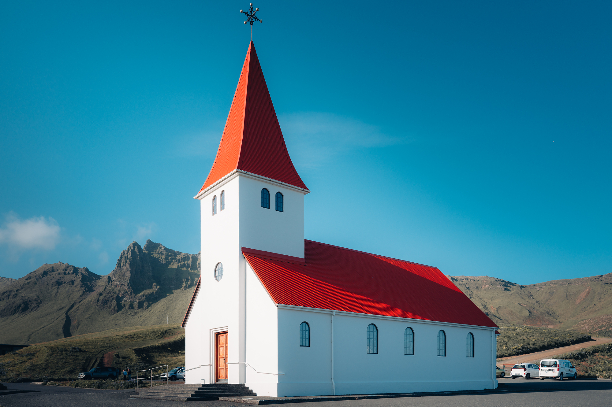 White church with a red roof set against a mountain landscape under a clear blue sky, photographed by Leon Eule.