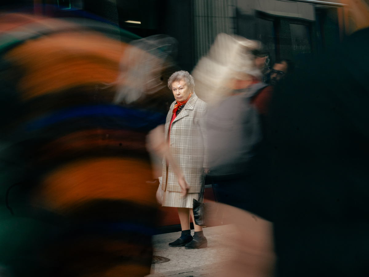 Capturing movement in photos with a still elderly woman in focus surrounded by blurred pedestrians in a busy street scene