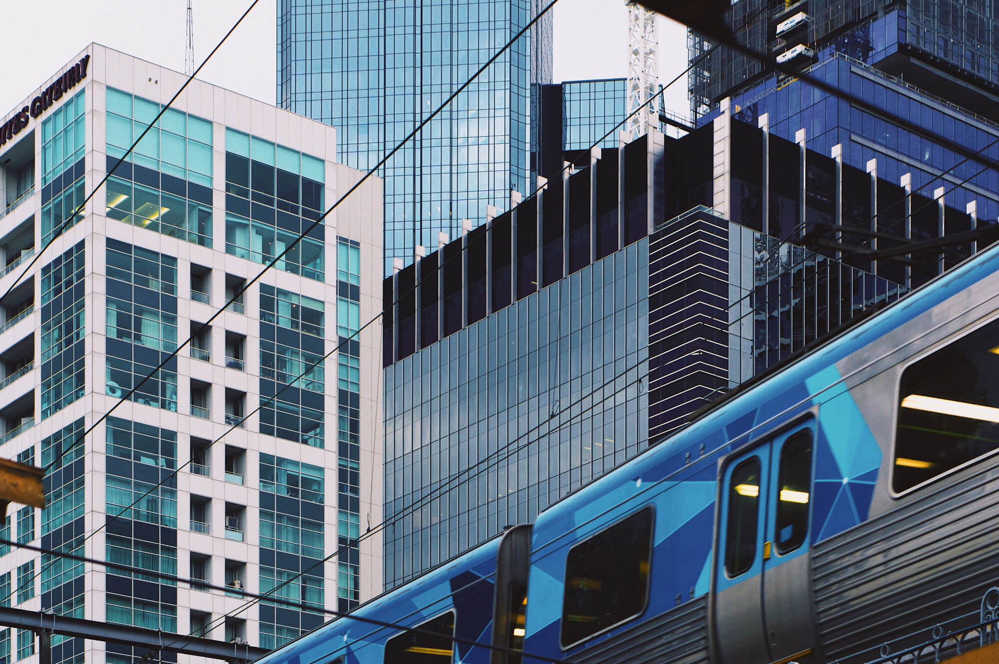Modern city architecture with a passing train, captured in a clean, geometric style reflecting the visual approach of Mikey Rogers.