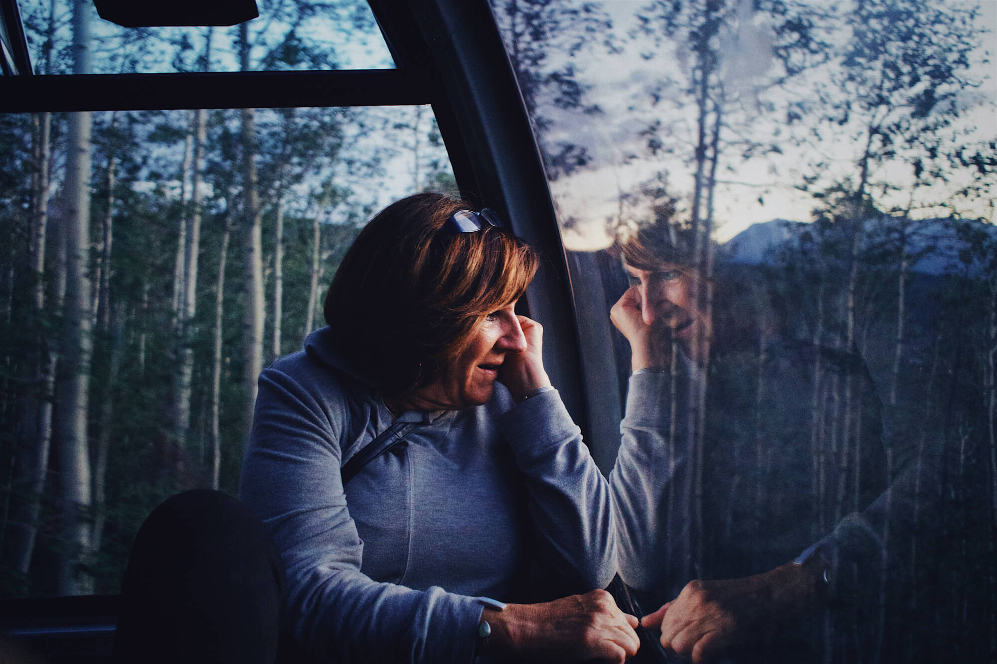 Woman gazing out a train window with her reflection, captured in an intimate, cinematic style inspired by Mikey Rogers.