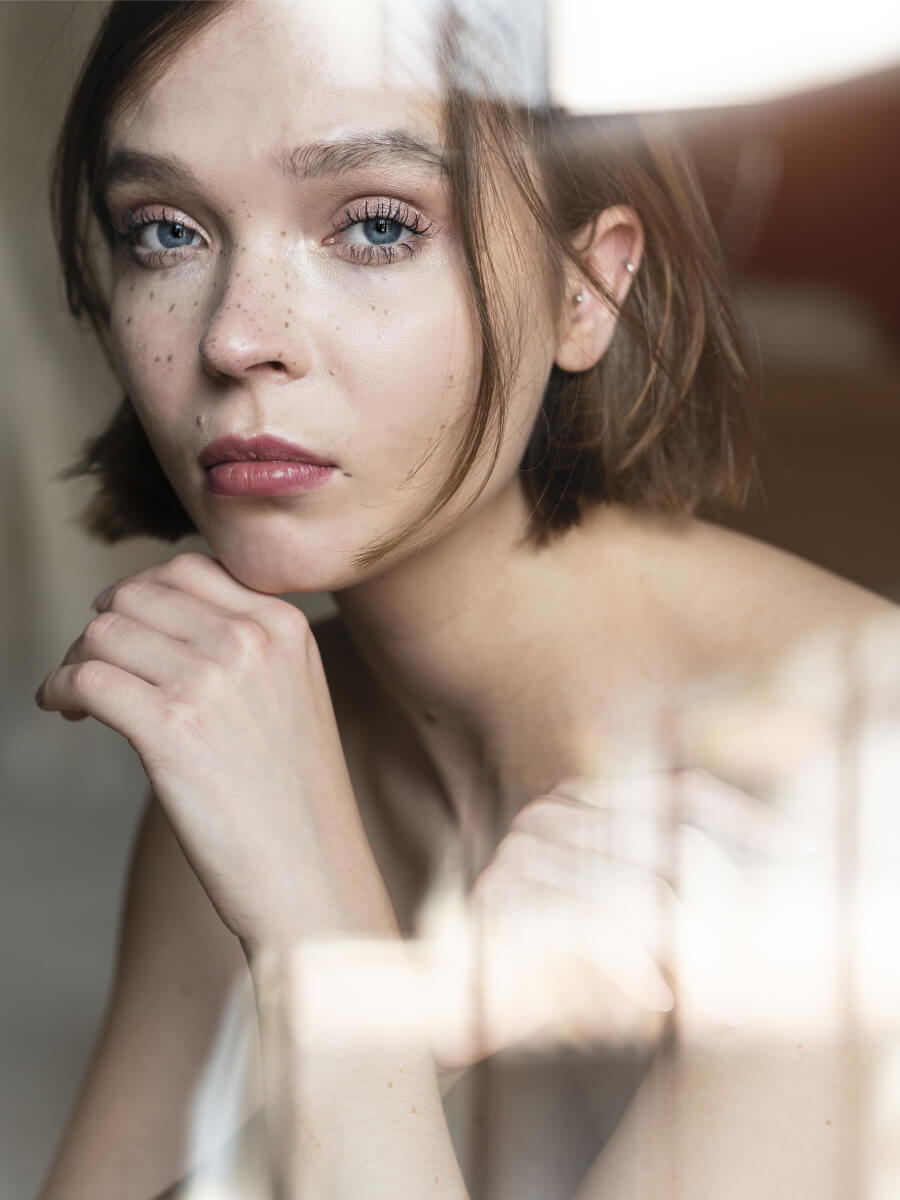 Freckled woman resting her chin on her hand in soft natural window light portrait photography.