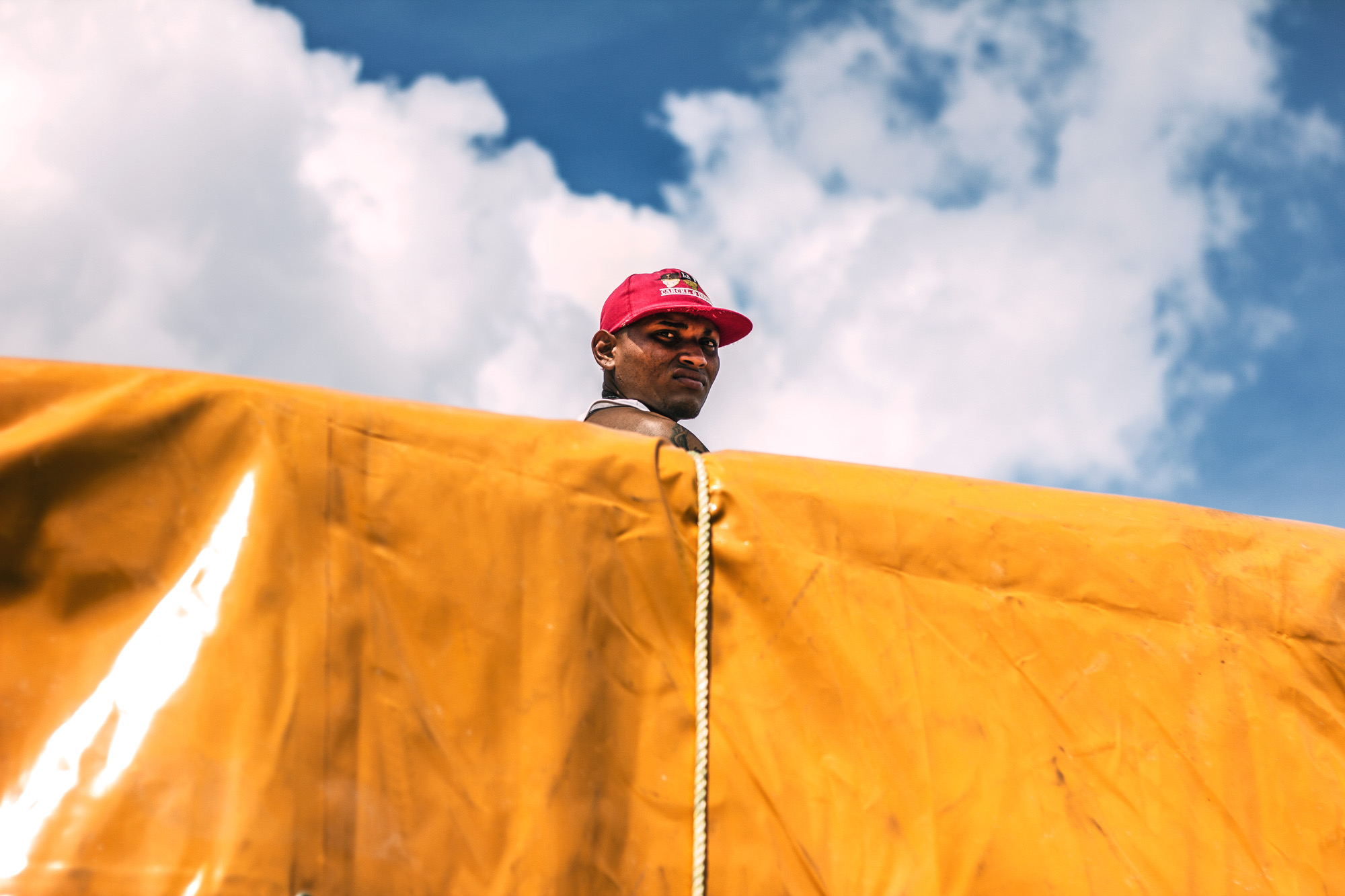 Man behind a yellow tarp against cloudy sky.