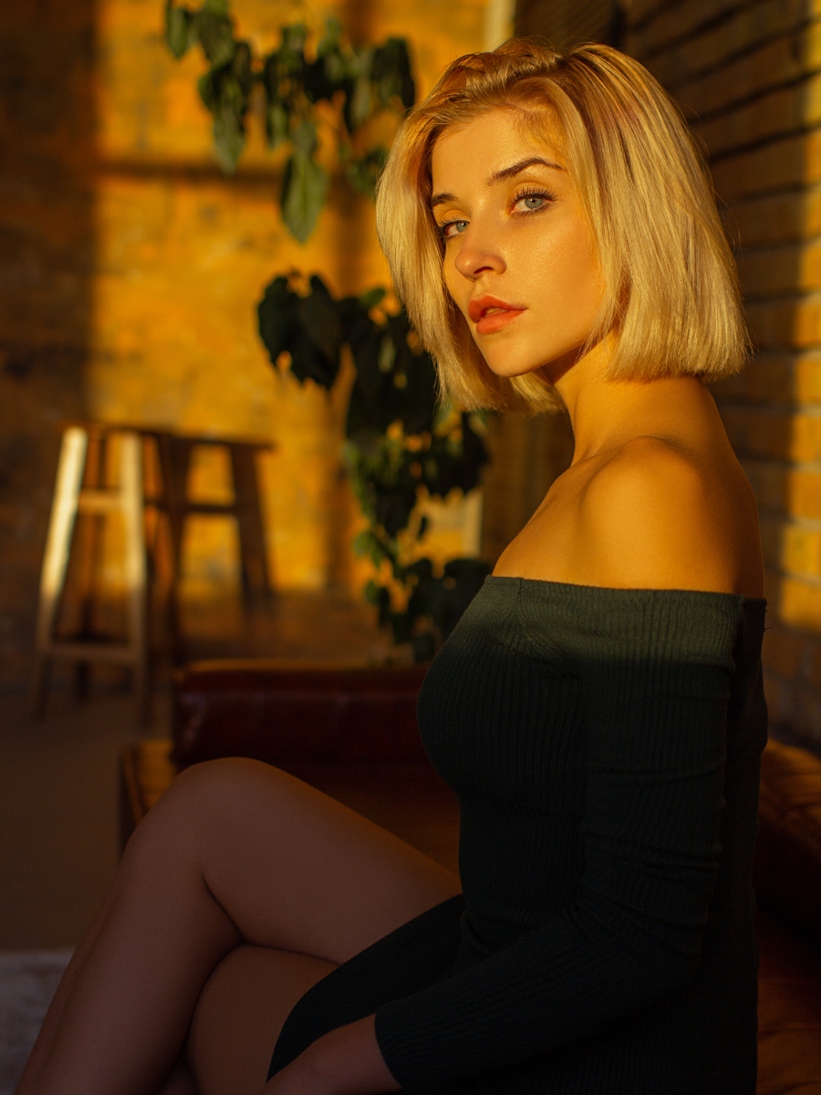 A documentary-style photography portrait of a woman bathed in warm golden hour light, seated in a rustic indoor setting with a contemplative gaze and natural shadow detail.