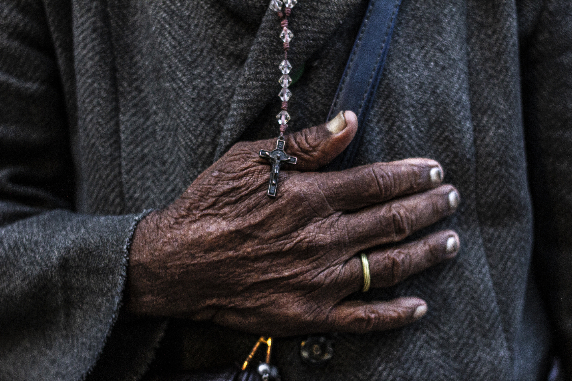 Weathered hand holding a crucifix necklace.