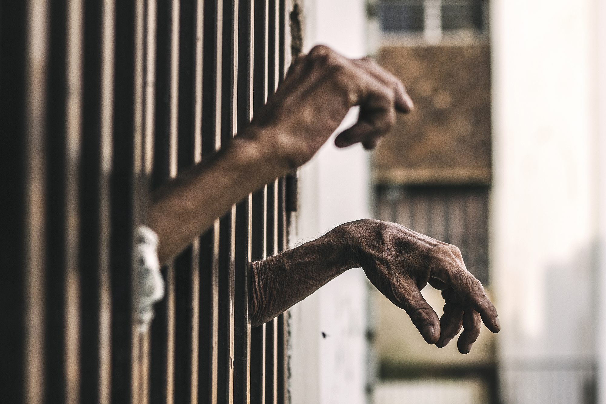 Two hands reaching out through metal bars.