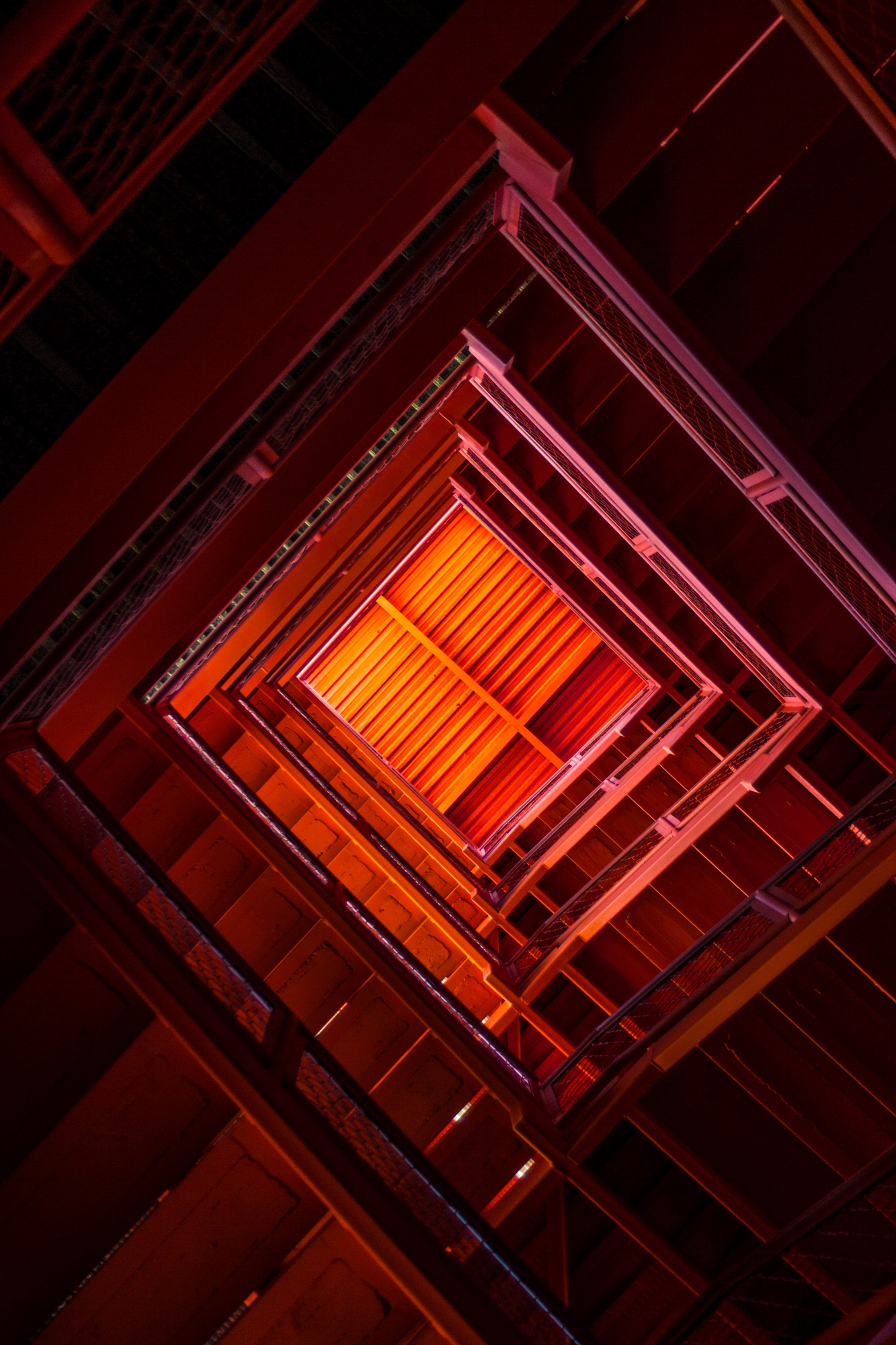 Looking up a red, illuminated geometric stairwell.