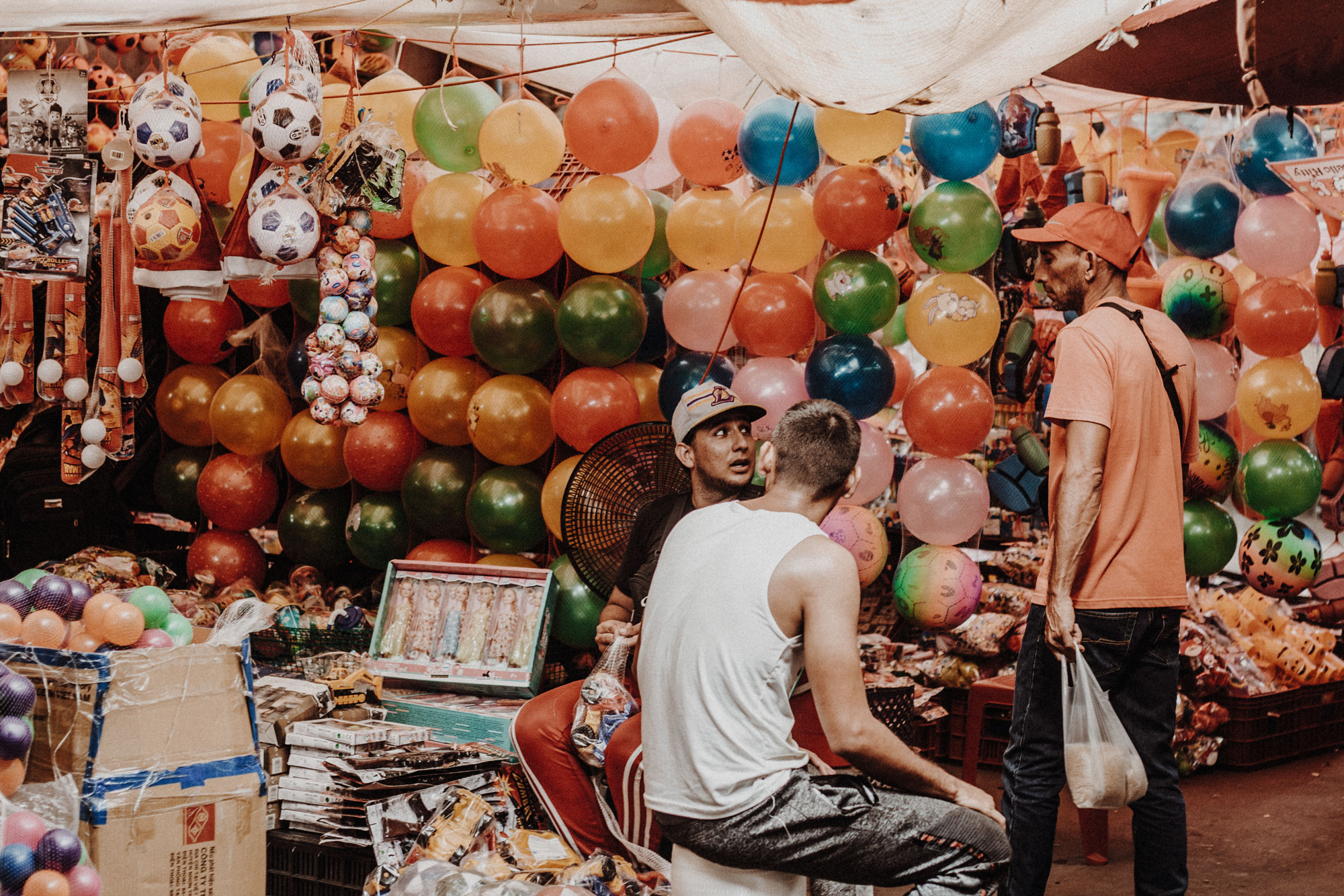 Two men talking in a market stall full of balloons.
