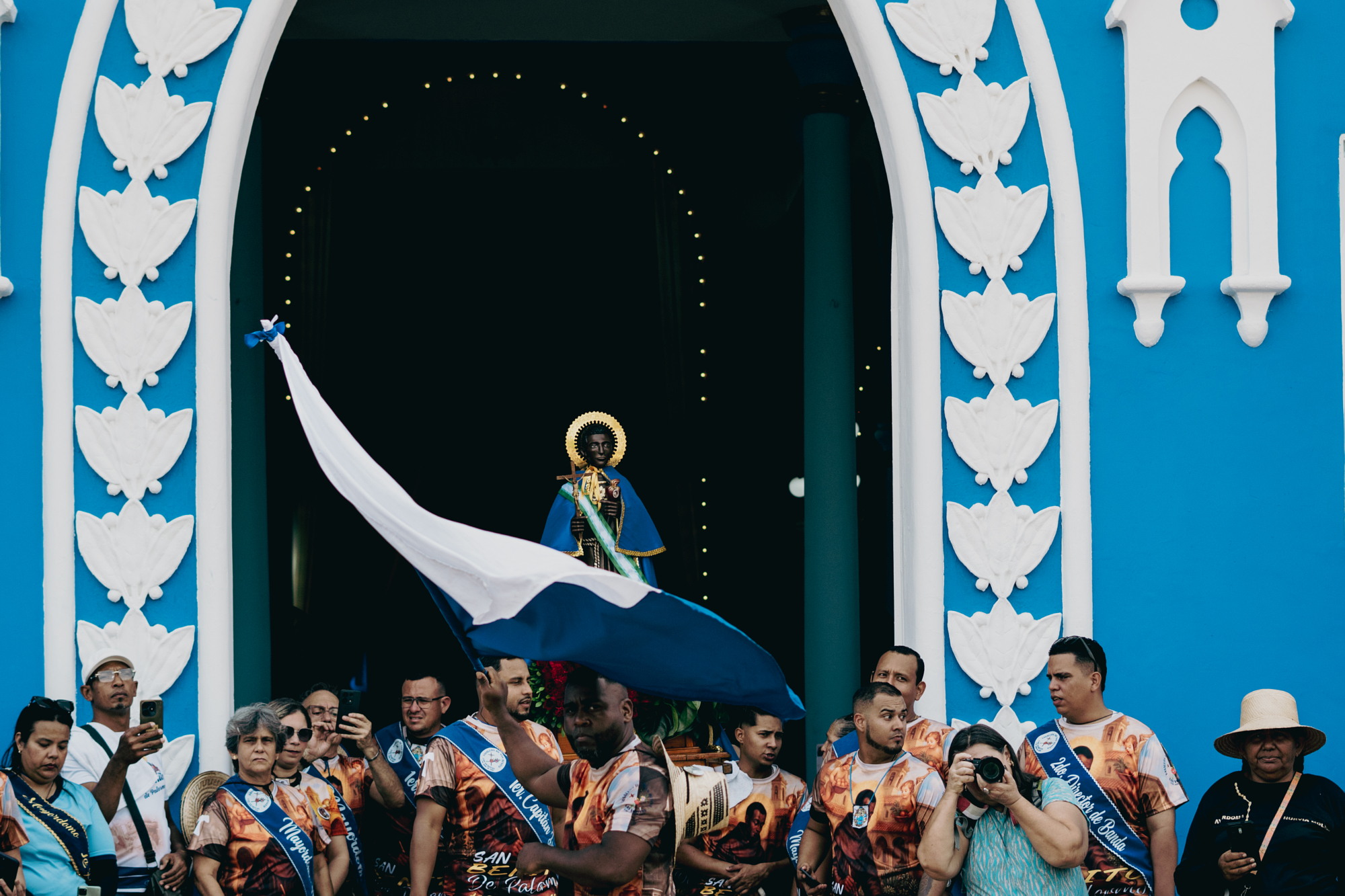 Religious procession outside a bright blue church in city.