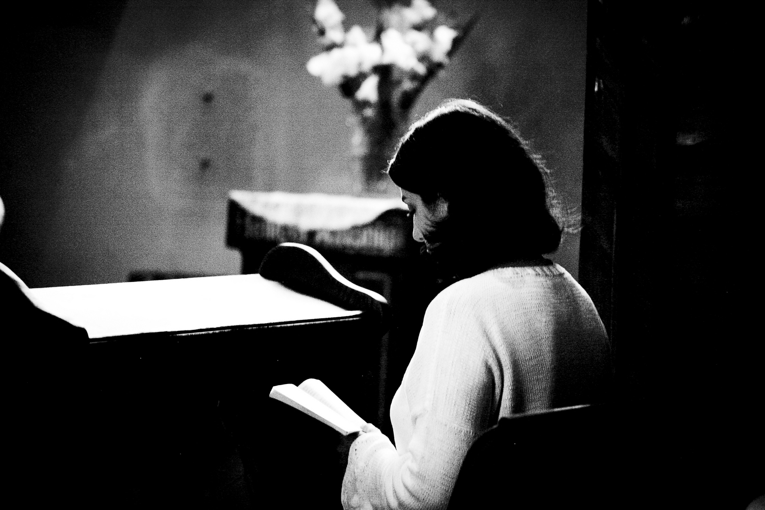 Moody photography of a woman looking down intently at a bible in a church.