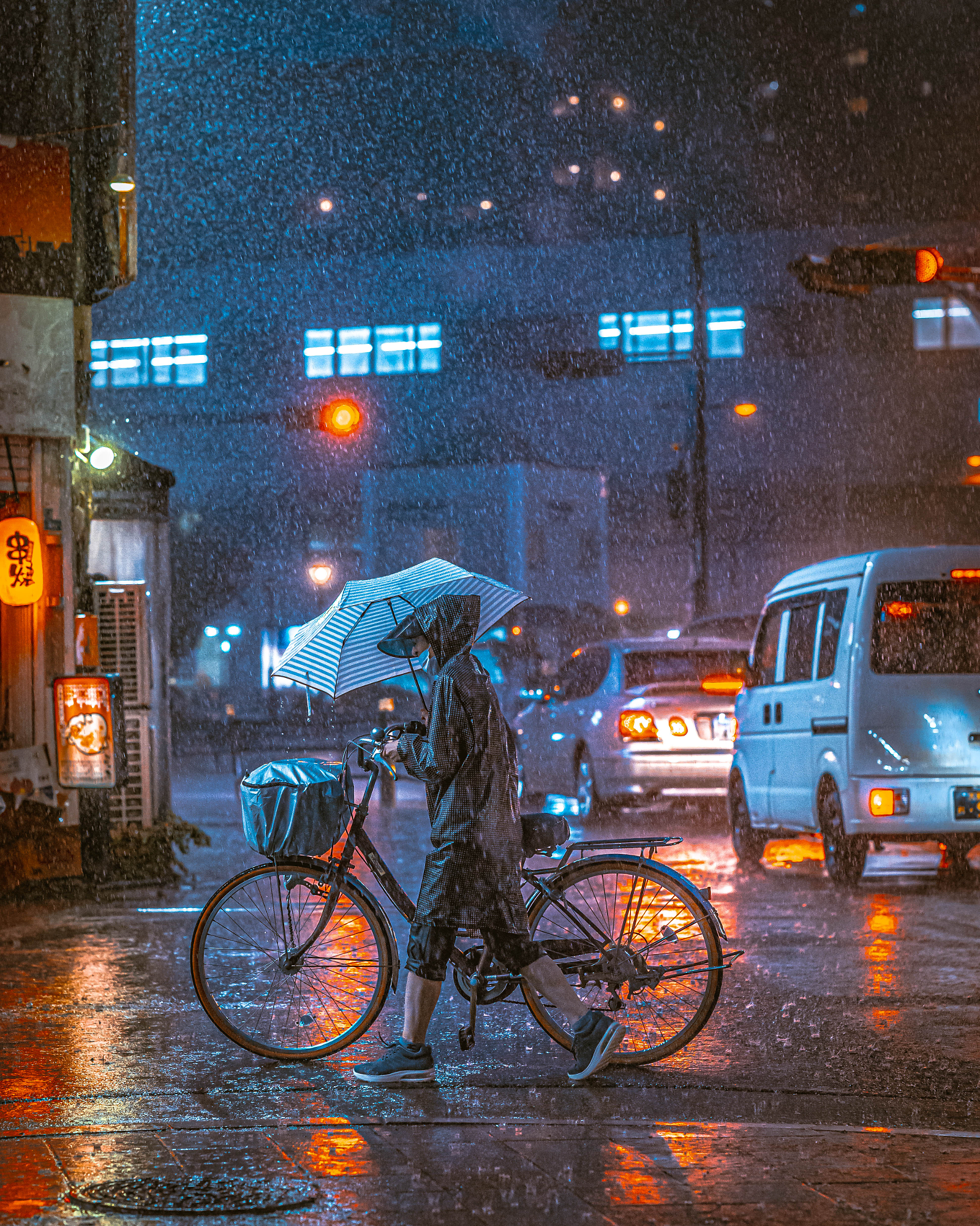 A cyclist in a raincoat pushes a bicycle across a wet street illuminated by neon lights and glowing red traffic signals, showcasing Masahiro Miyagi street photography.