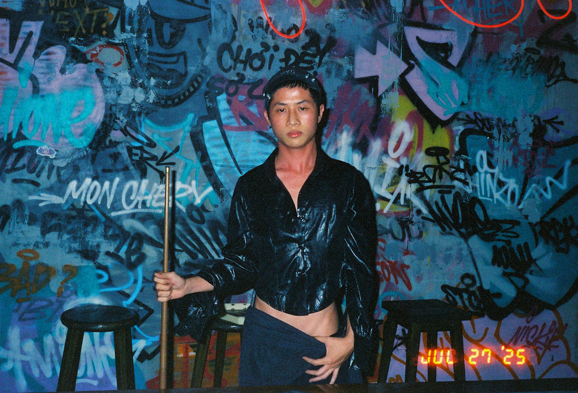 Southeast Asia street photography portrait of a man standing in front of a colorful, heavily graffitied wall on analog film.