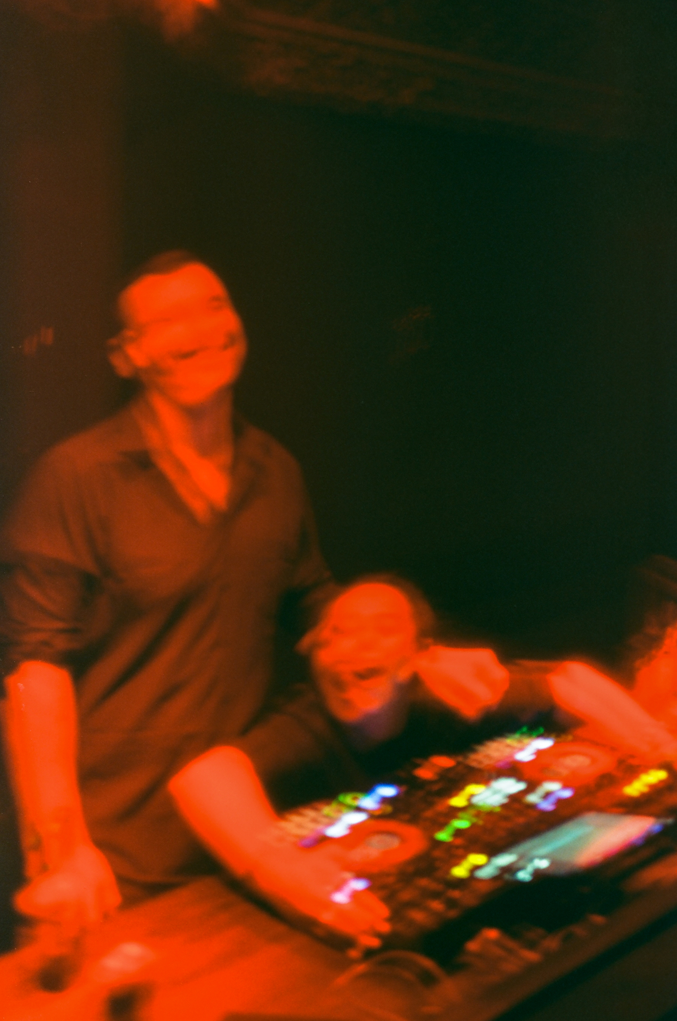 Motion blur night photography film capturing two friends laughing and sharing an authentic human connection behind DJ decks.