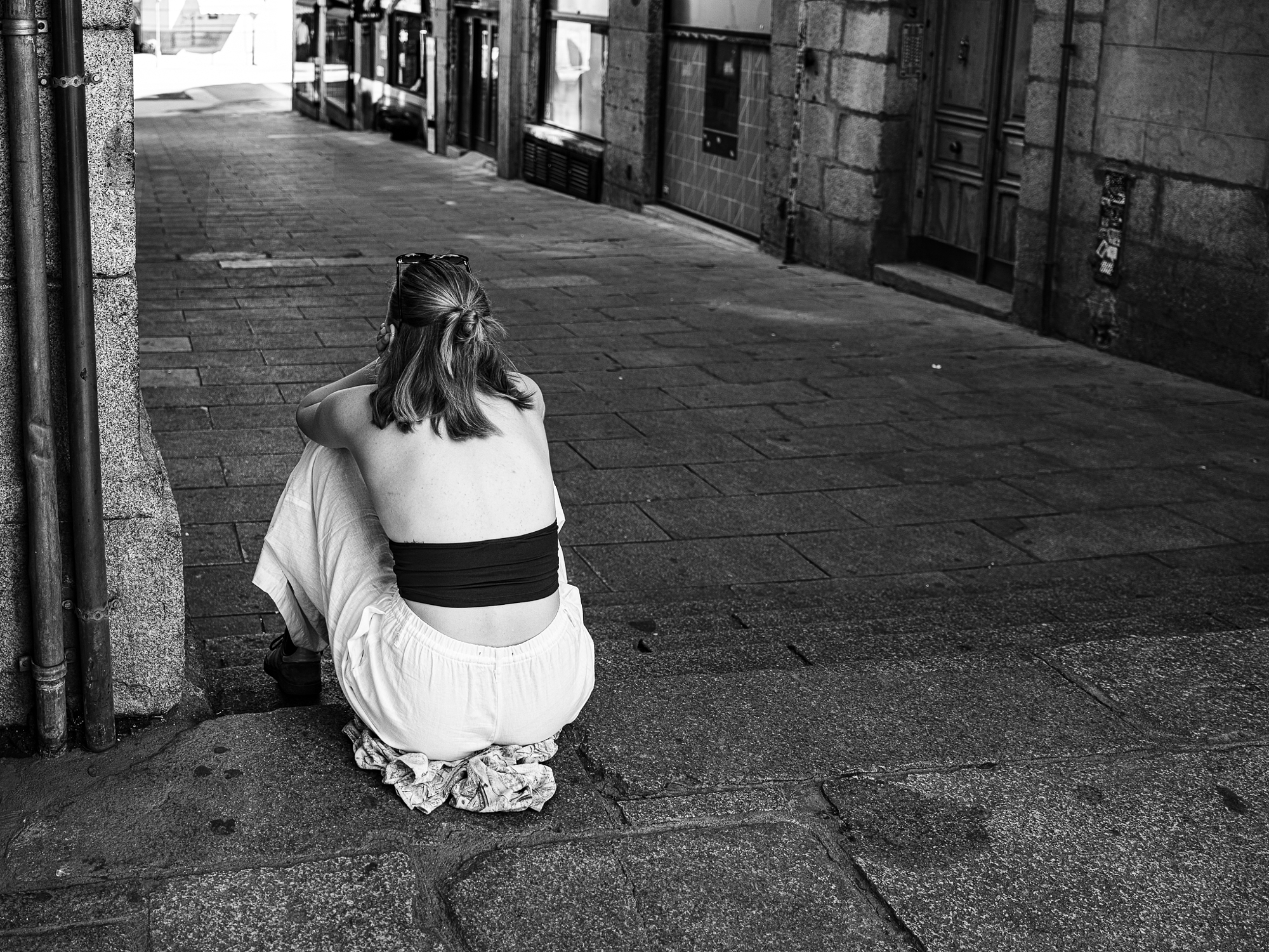 Urban photography of a woman in a traditional dress sitting on a curb, captured by Enrique Murciano.