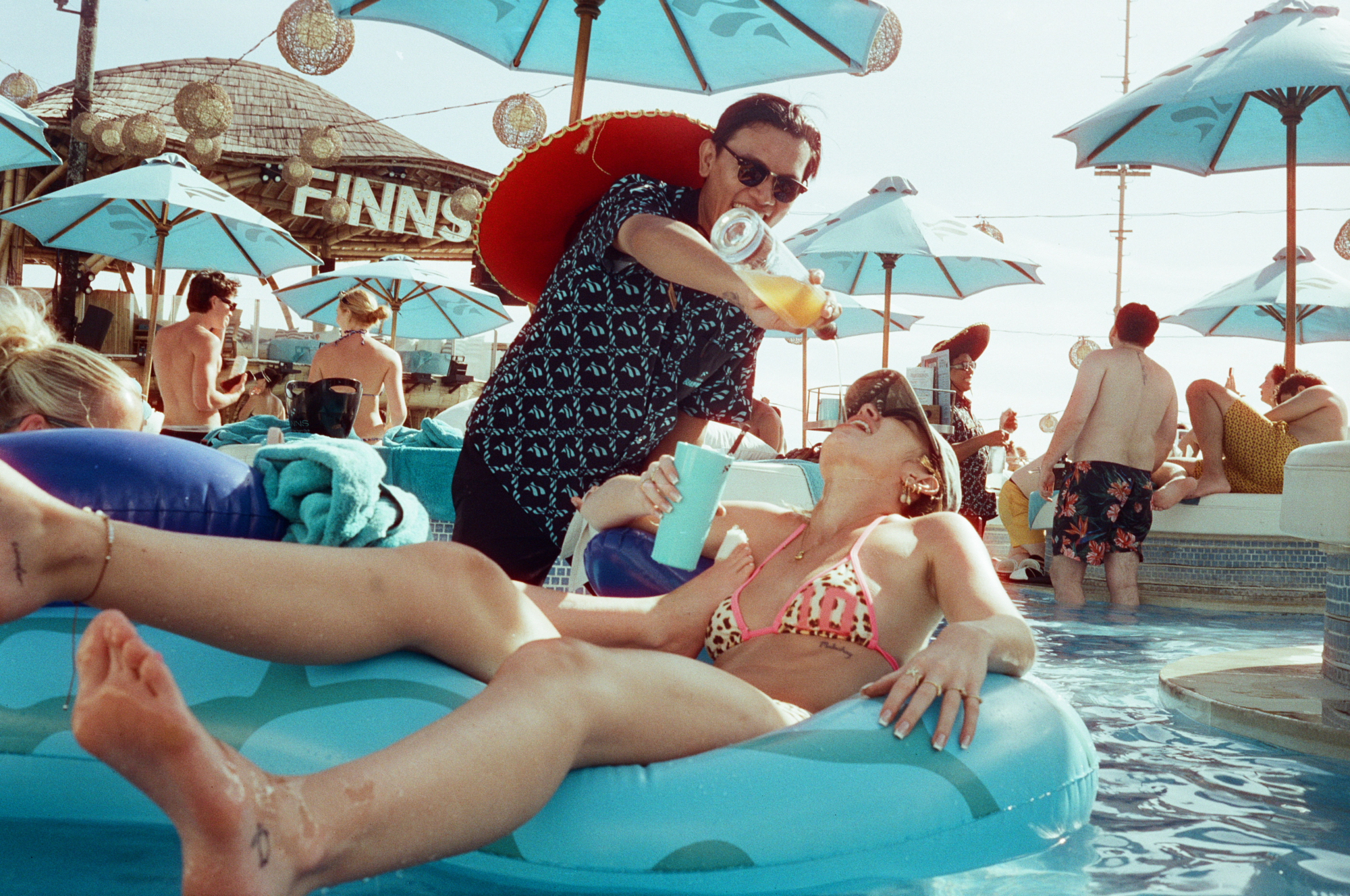 Spontaneous 35mm film photo of friends laughing and drinking poolside at Finns Beach Club in Bali.