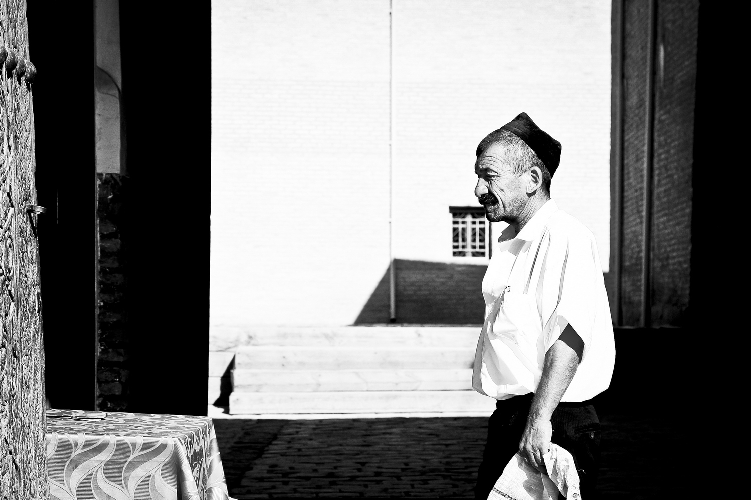 Black and white street photography portrait of an elderly man walking in high-contrast light.