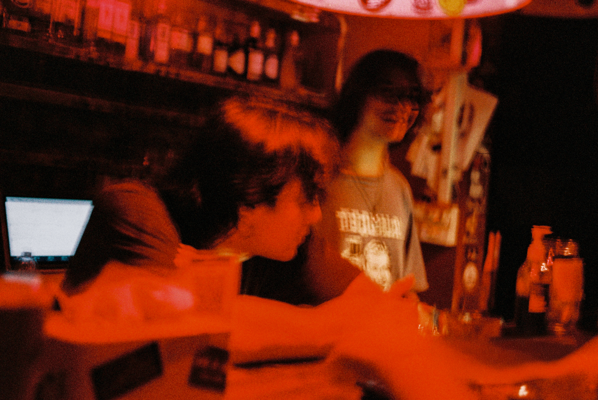 Candid night photography film of bartenders working behind a bar counter under heavy red neon ambient lighting by Katerina Shishkina.