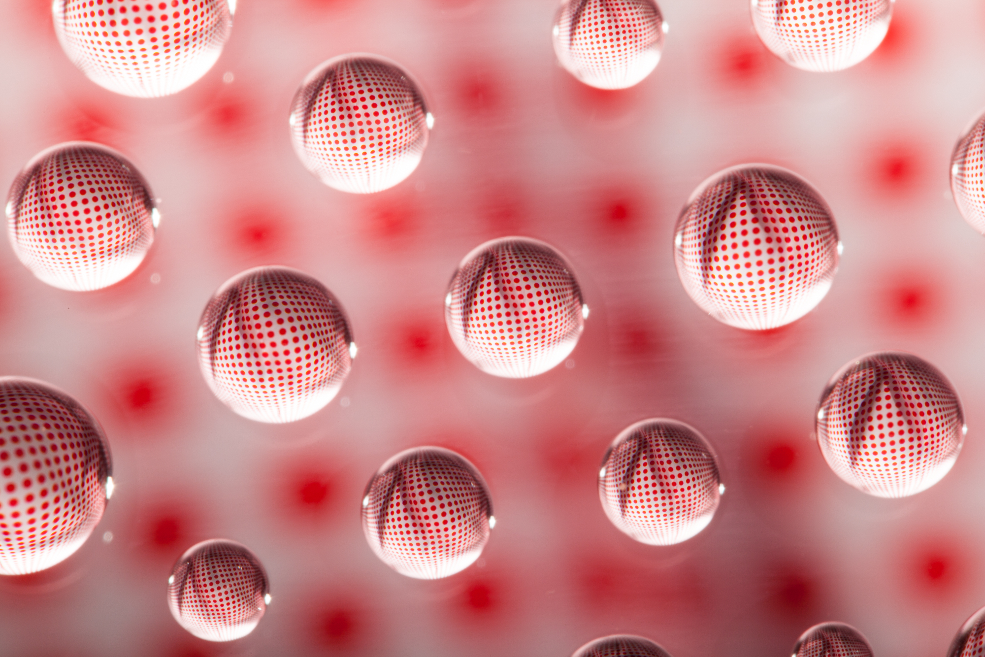 Creative macro photography ideas showcasing clear water droplets acting as lenses to refract a pattern of red polka dots.