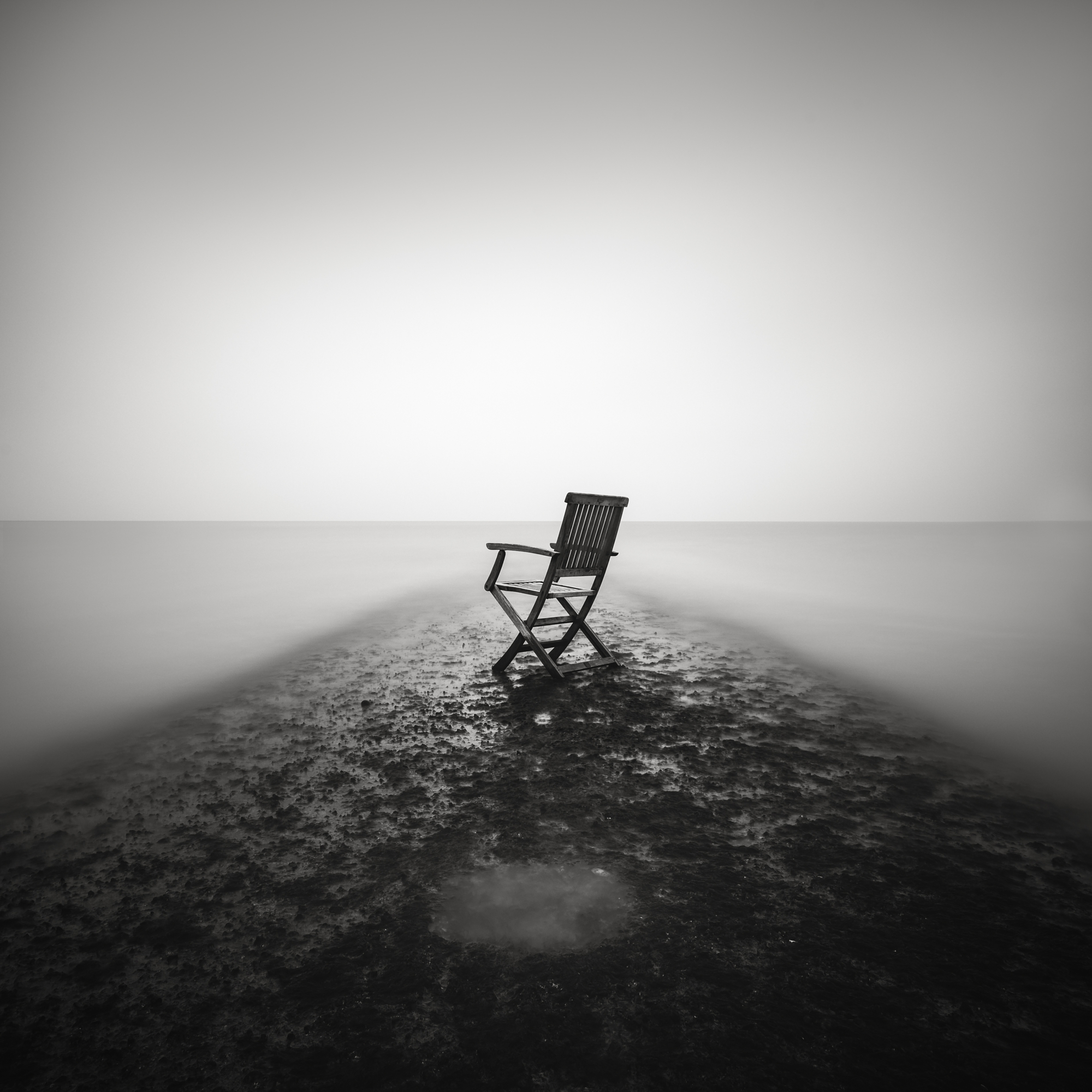 Minimalist long exposure photography of a lone chair on a misty jetty.