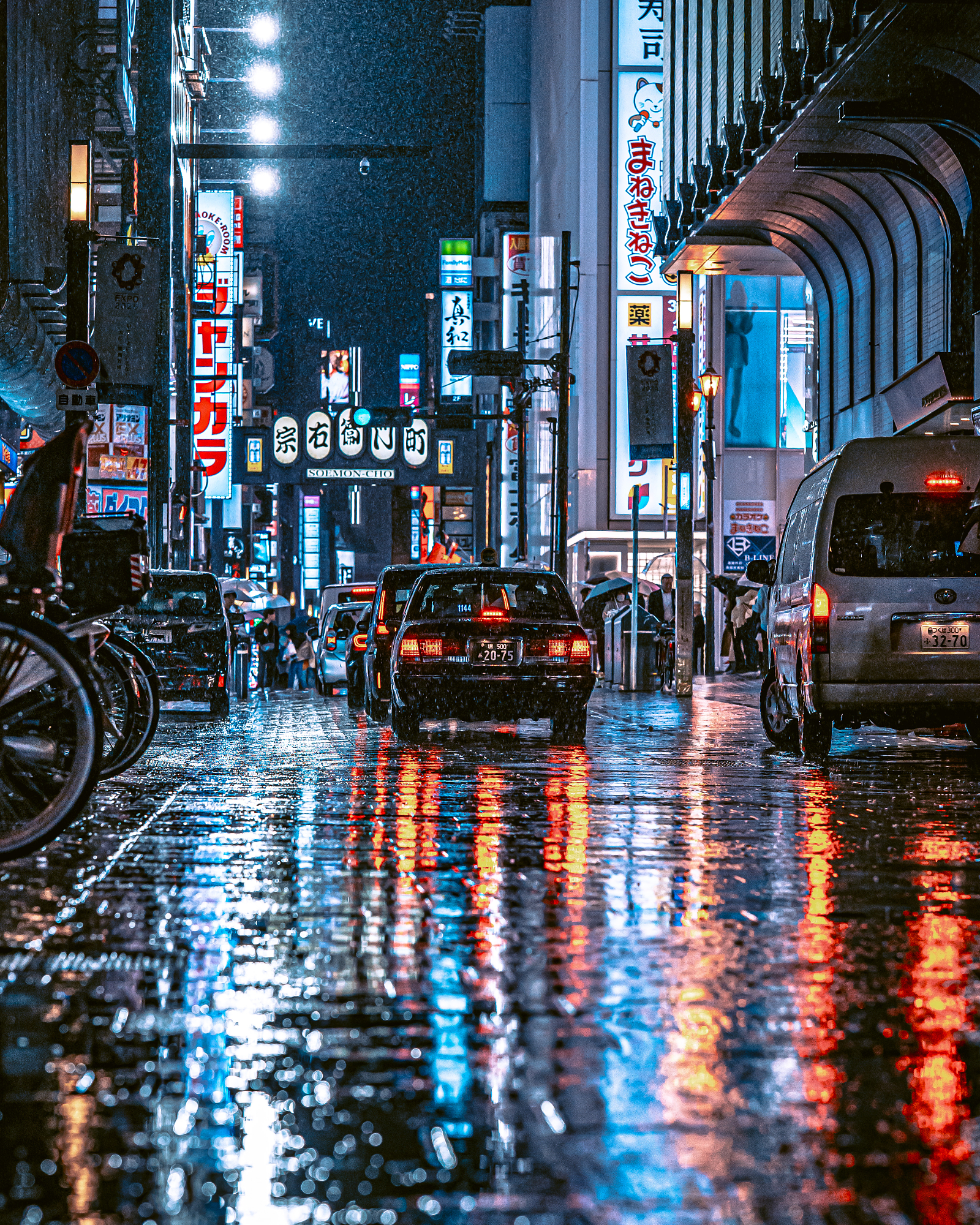 A taxi drives through a bustling, neon-lit commercial district in the rain, highlighting the intense, moody atmosphere typical of Tokyo street photos.
