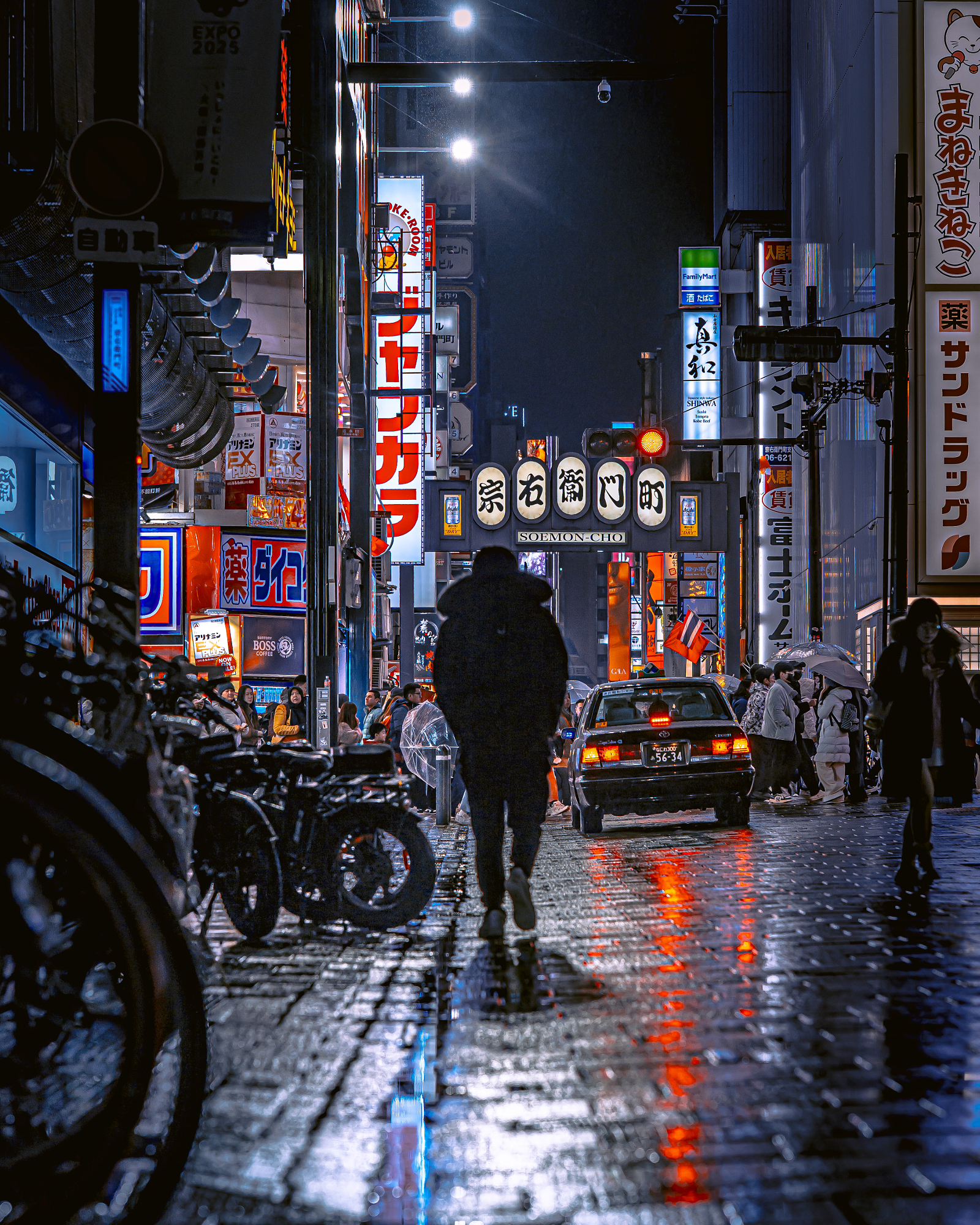 A lone figure in a heavy winter coat walks down a wet, highly reflective street lined with massive, colorful neon billboards, capturing the essence of Masahiro Miyagi street photography.