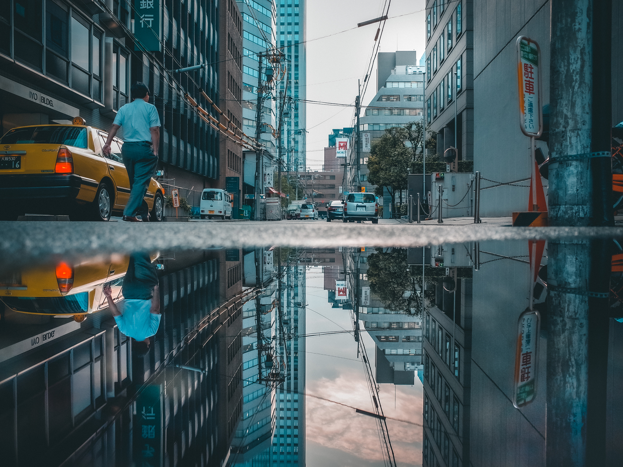 A businessman walks past a yellow taxi cab, his figure perfectly mirrored in a large puddle on the street, illustrating the symmetry found in cinematic urban photography.