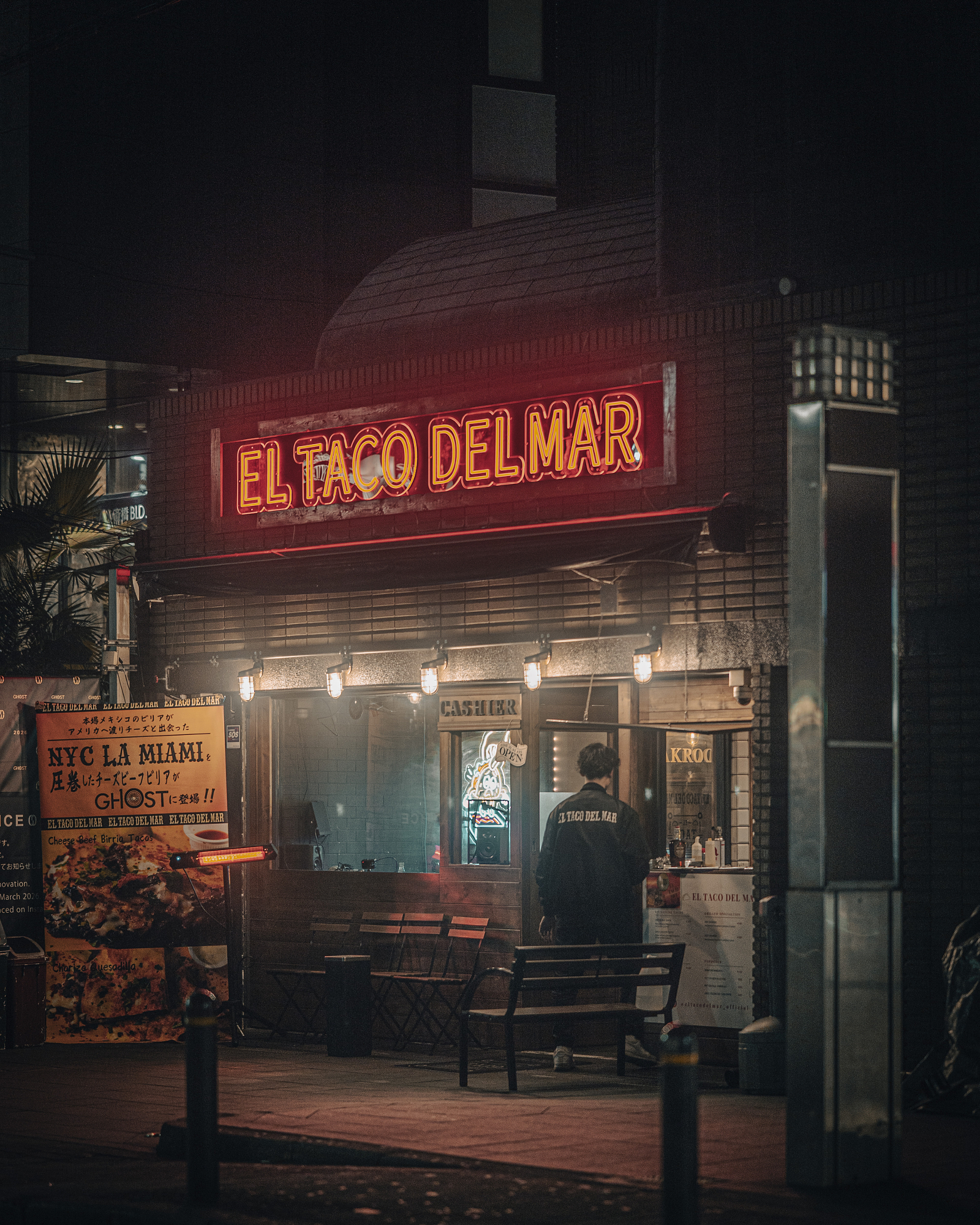 A person standing outside a restaurant with bright red neon signage at night, framed beautifully using compression in 85mm street photography.