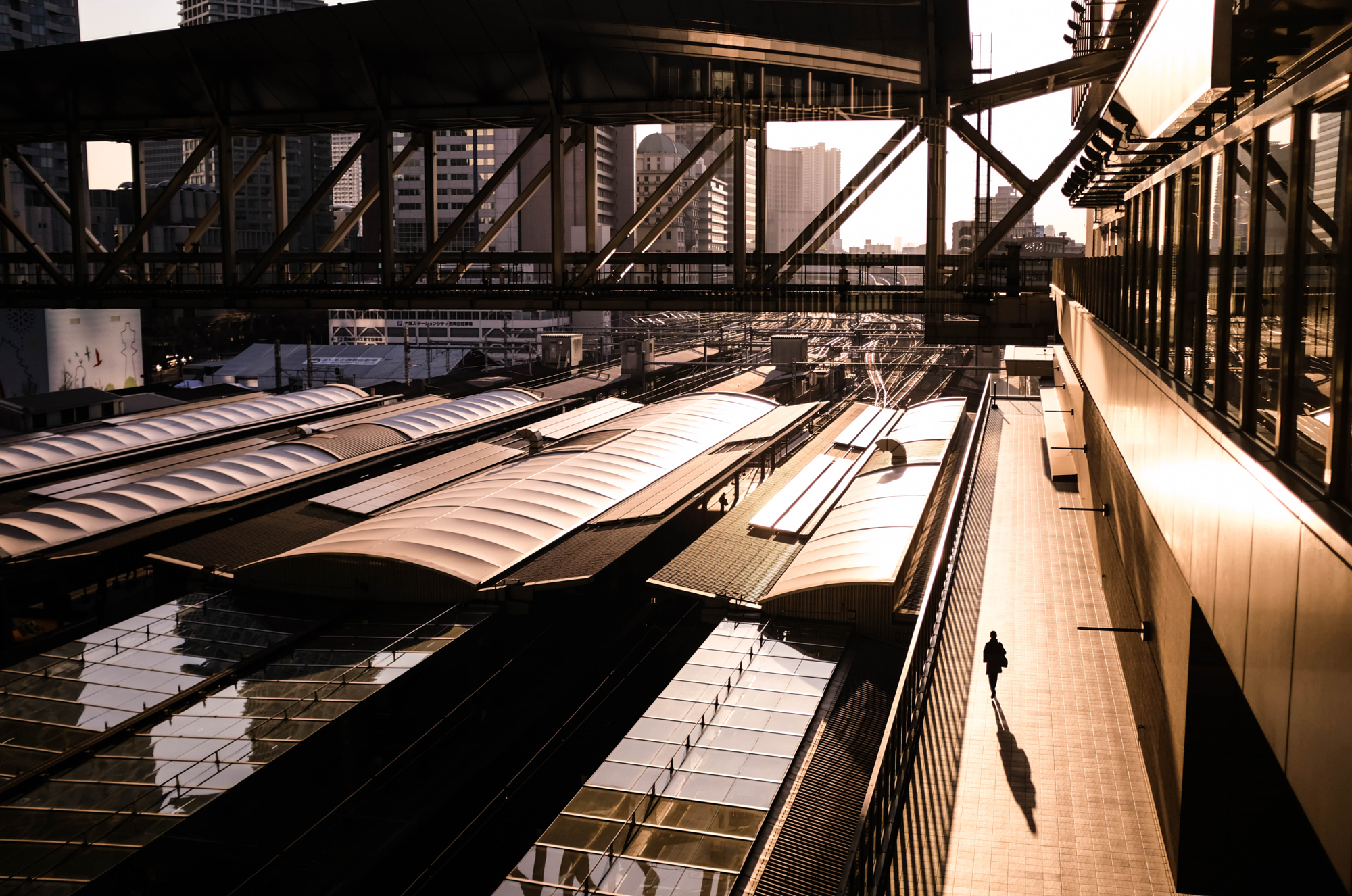 High-angle golden hour view of an urban railway station walkway with a lone traveler casting a long shadow, highlighting Masahiro Miyagi street photography style.