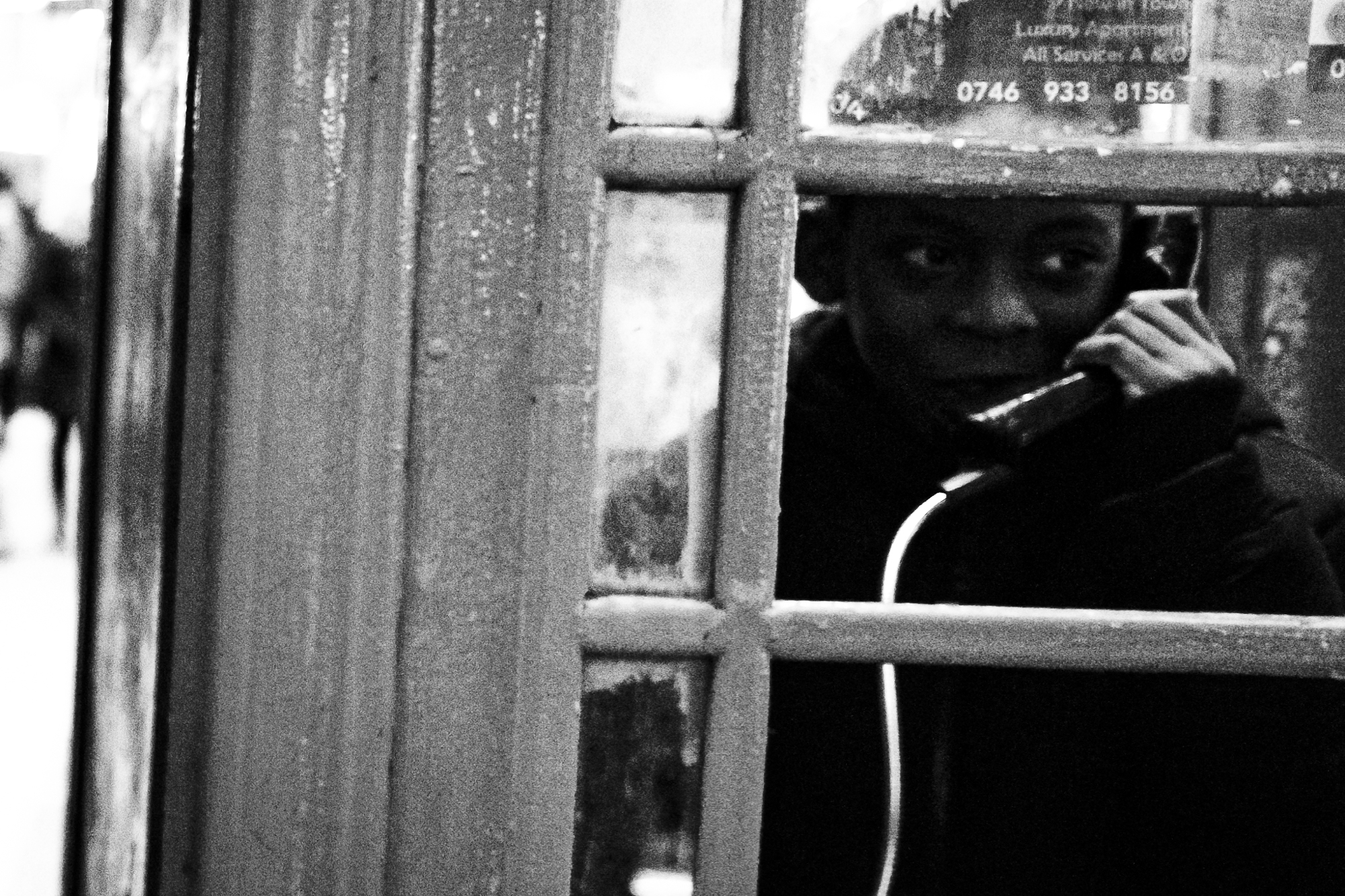 Enrique Murciano street photography featuring a person talking in a phone booth.