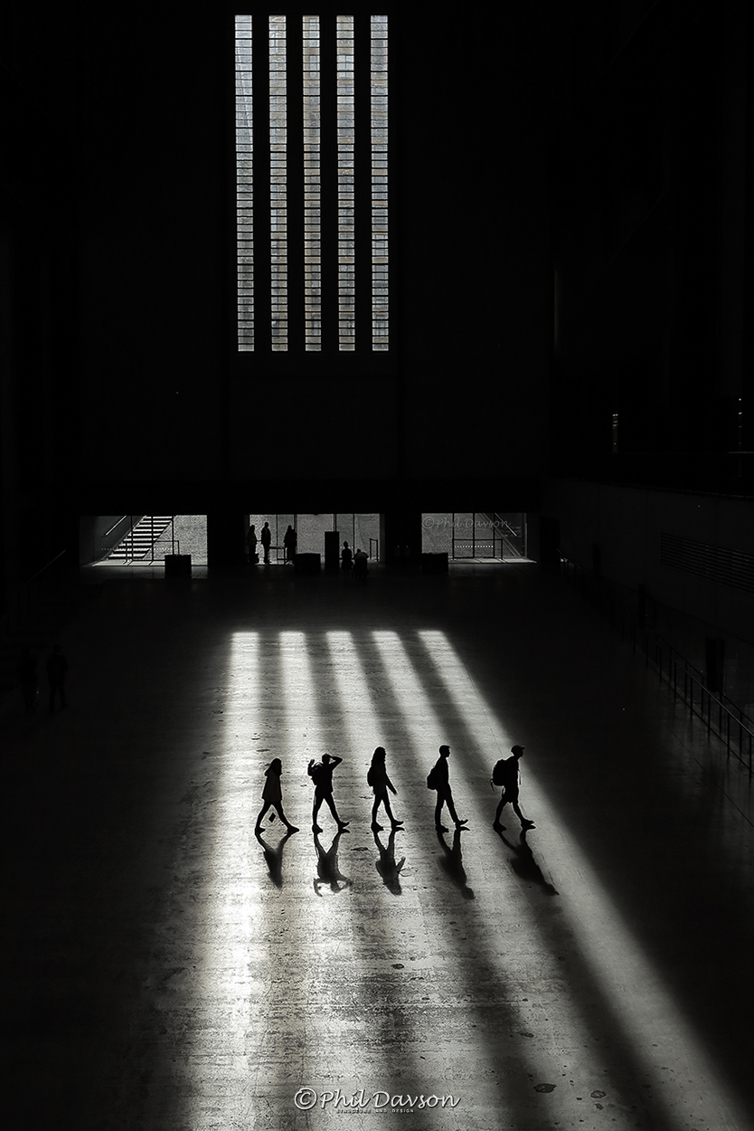 Silhouette shadows of people walking across a light beam at the Tate Modern art gallery in London.