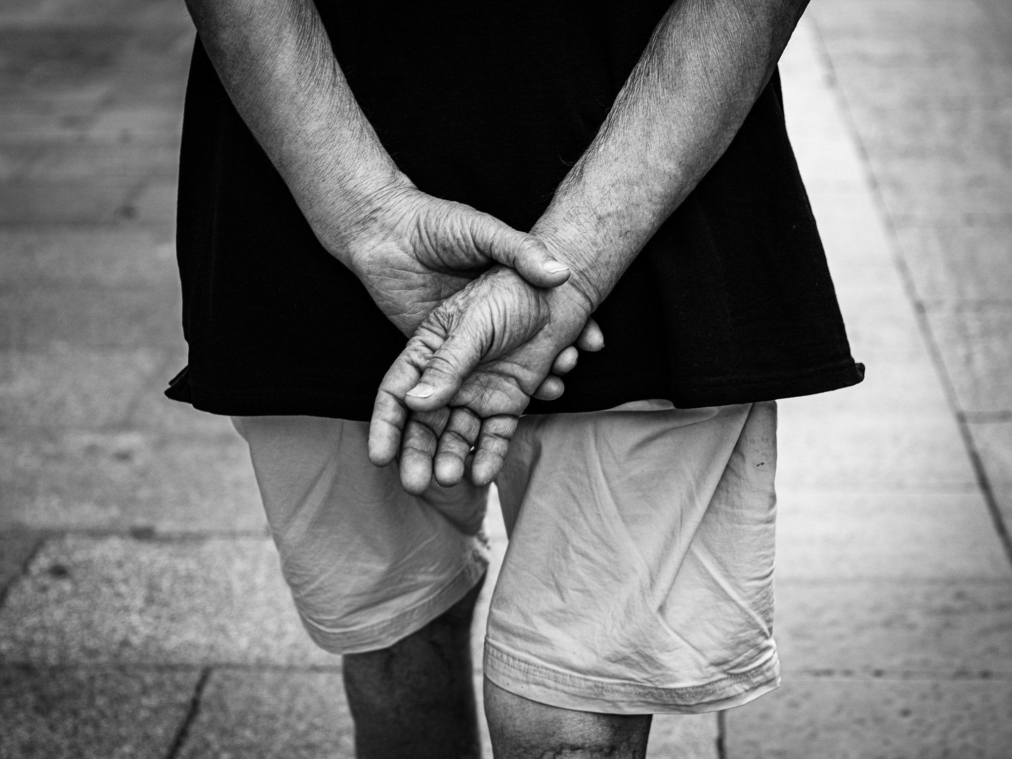 Minimalist black and white street photography focusing closely on a person’s crossed hands.
