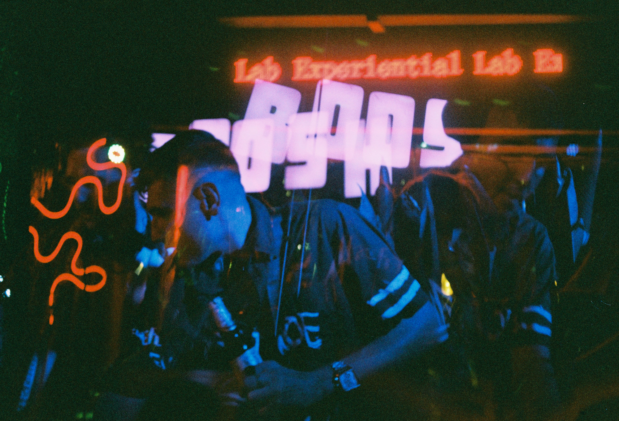 Experimental double exposure on 35mm film photography depicting crowds at a dark night venue with glowing signs.