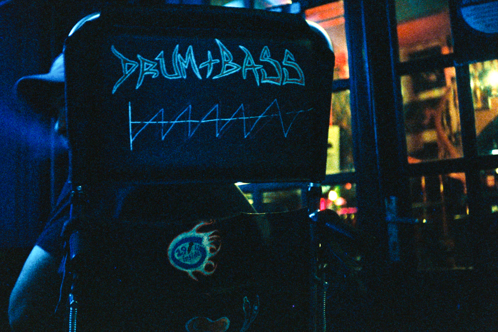 Katerina Shishkina photography of a wheelchair with "Drum + Bass" chalk lettering at a nightlife music event.