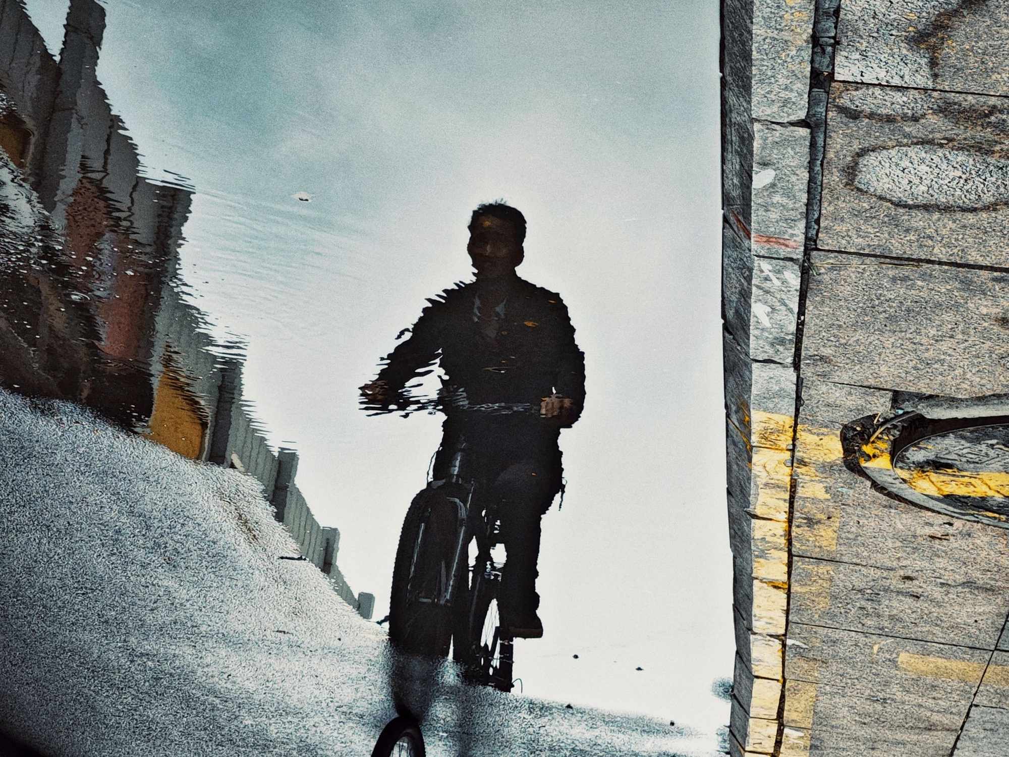 Reflection of a cyclist riding down a street in a puddle, demonstrating puddle photography tips after rain.