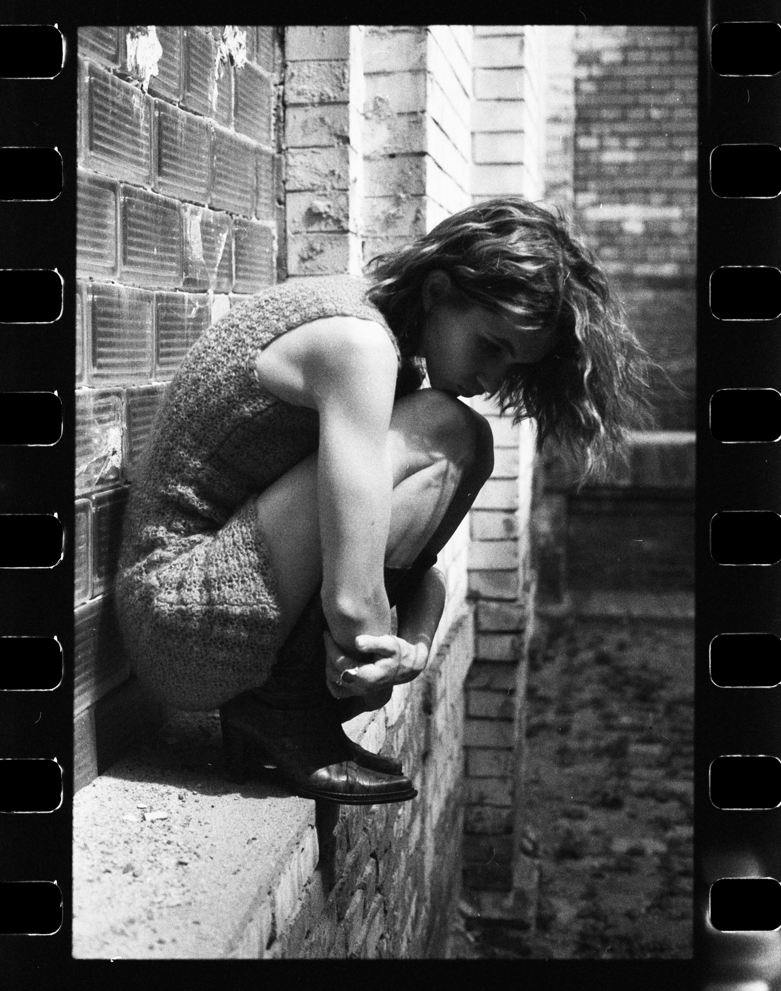 35mm analog film black and white portrait by Holger Nitschke featuring a woman crouching on a brick ledge.