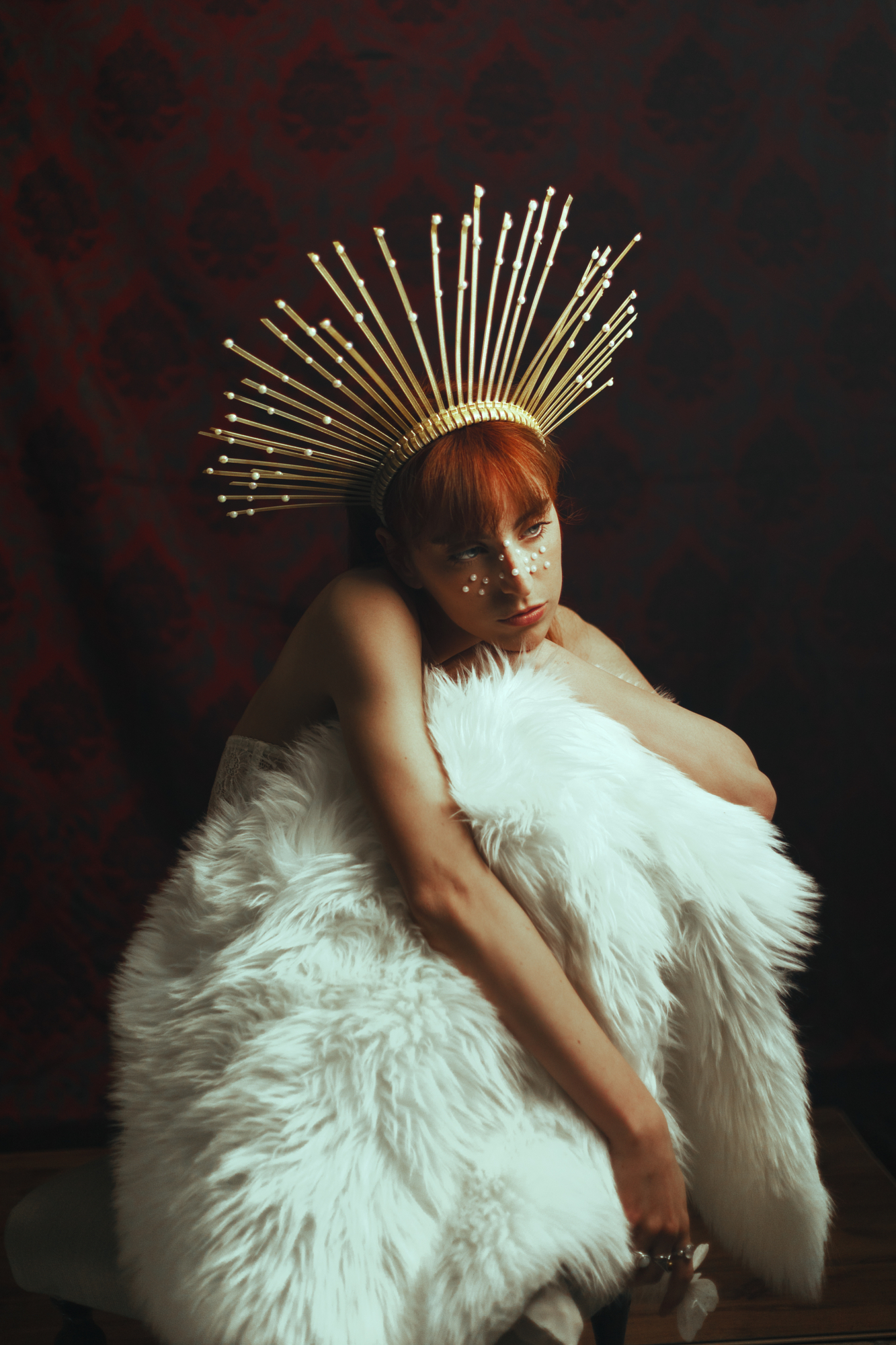 Dramatic painterly fashion photography featuring a model wearing a gold sunburst crown and rich faux fur with deep chiaroscuro contrast.