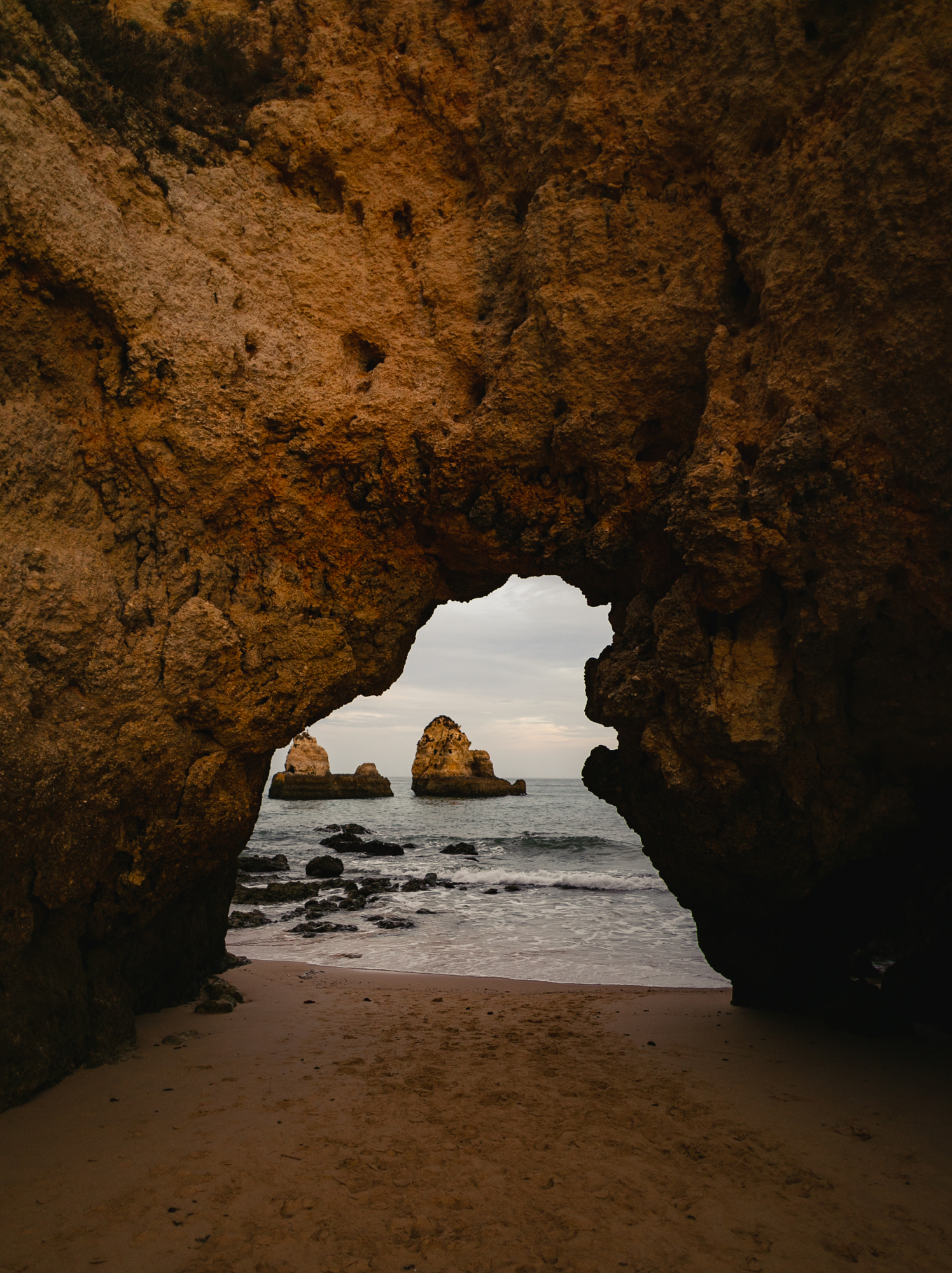 Coastal rock arch framing sea stacks on a beach near Lisbon, captured by David Velez photography.