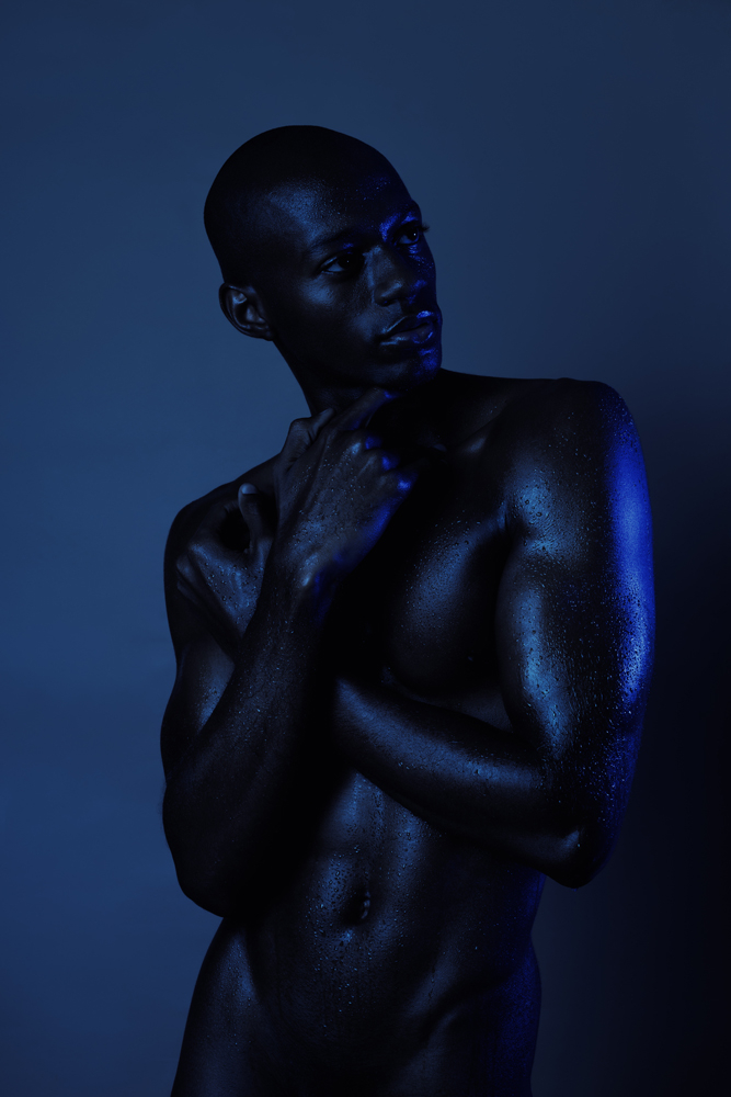 Artistic studio portrait of a shirtless man under deep blue artificial light, capturing the anatomy and male form photo series by David Velez.