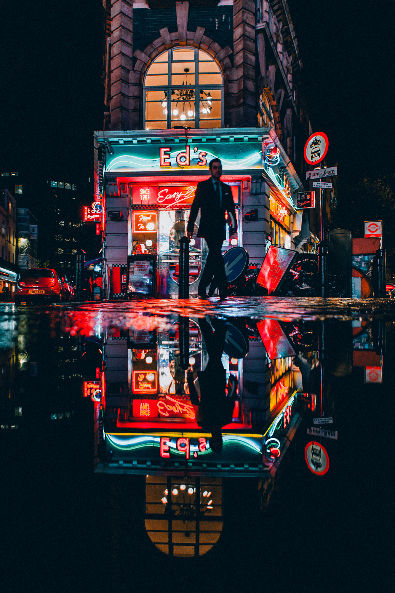 Vibrant neon diner lights mirrored in a wet street puddle, demonstrating urban street photography composition at night.