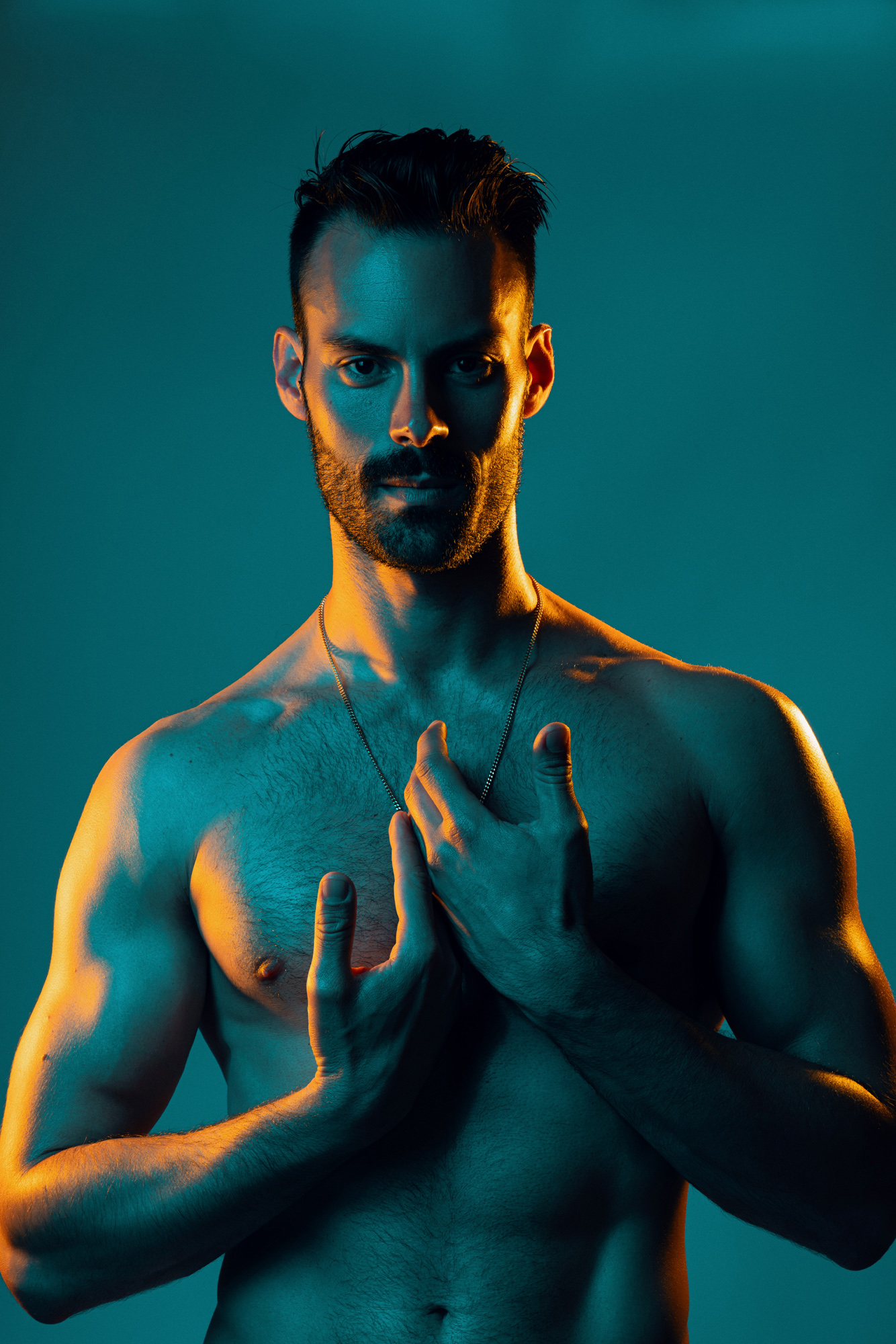 Studio portrait of a shirtless man illuminated by vibrant orange and teal lighting, highlighting the Golden Boys male form photo series by David Velez photography.