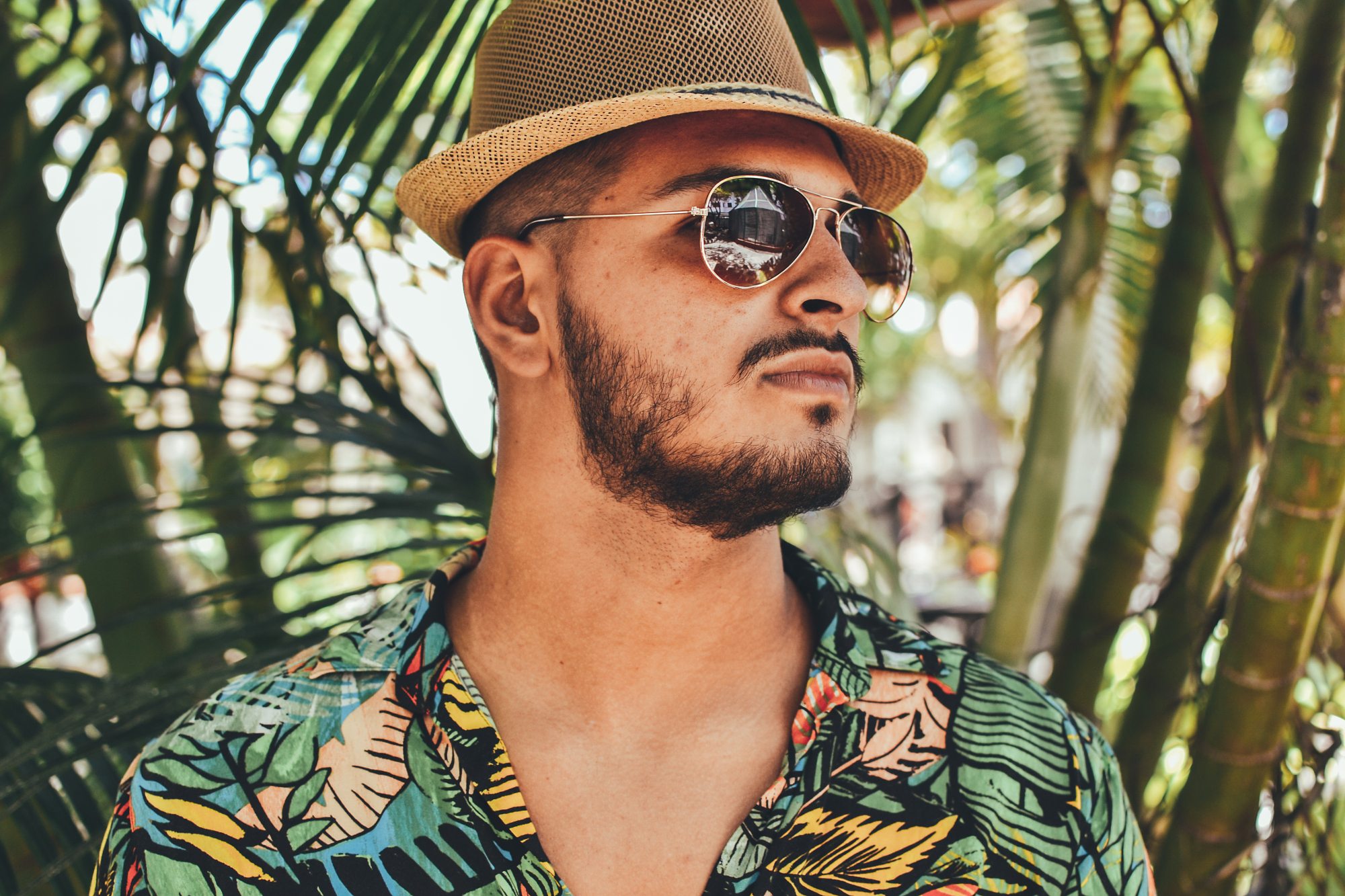 A man wearing a fedora and a tropical print shirt in front of palm trees, showcasing natural photo editing and rich outdoor photography colors.