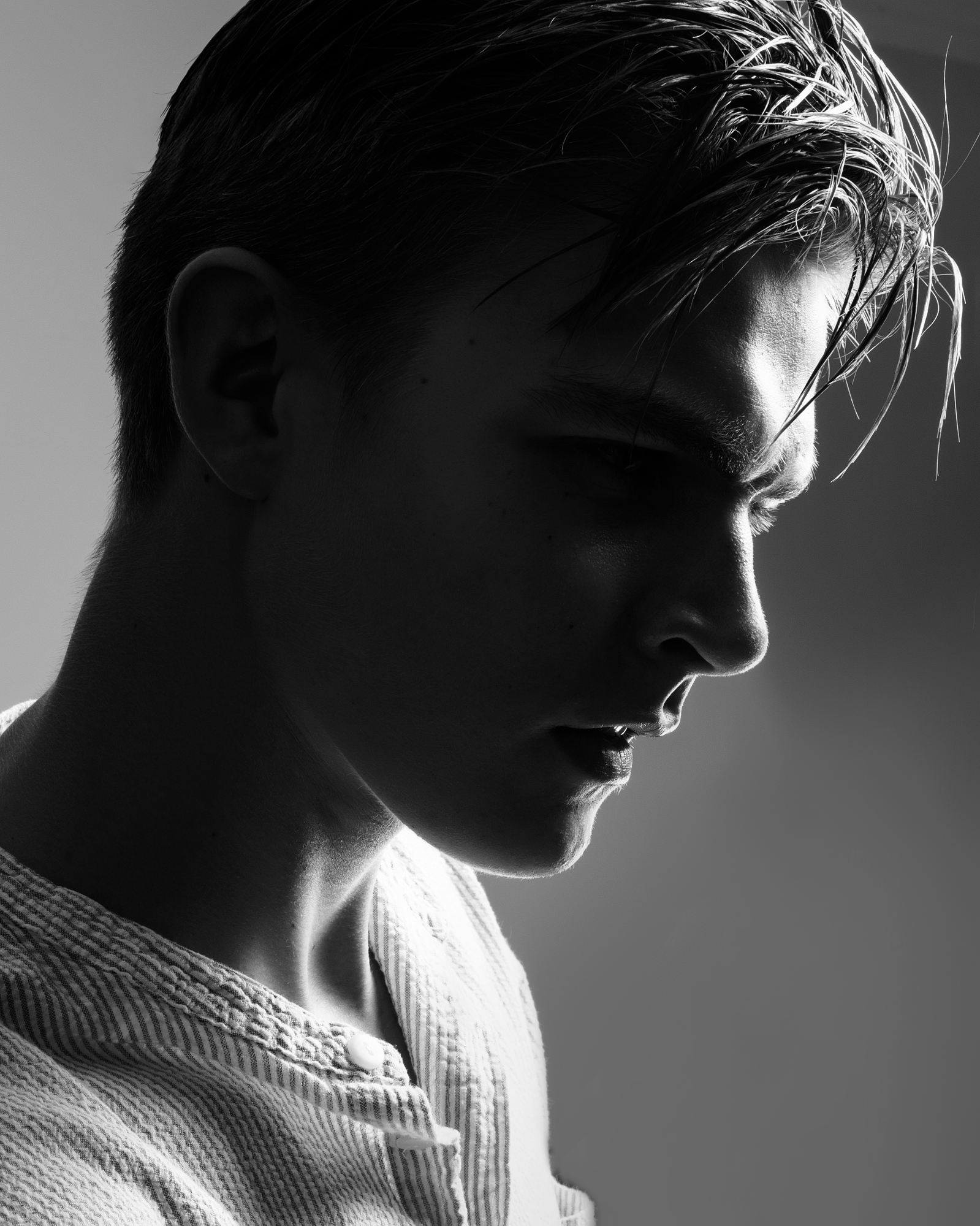 Dramatic black and white close-up portrait of a man with high-contrast rim lighting, an example of male beauty photography by David Velez.