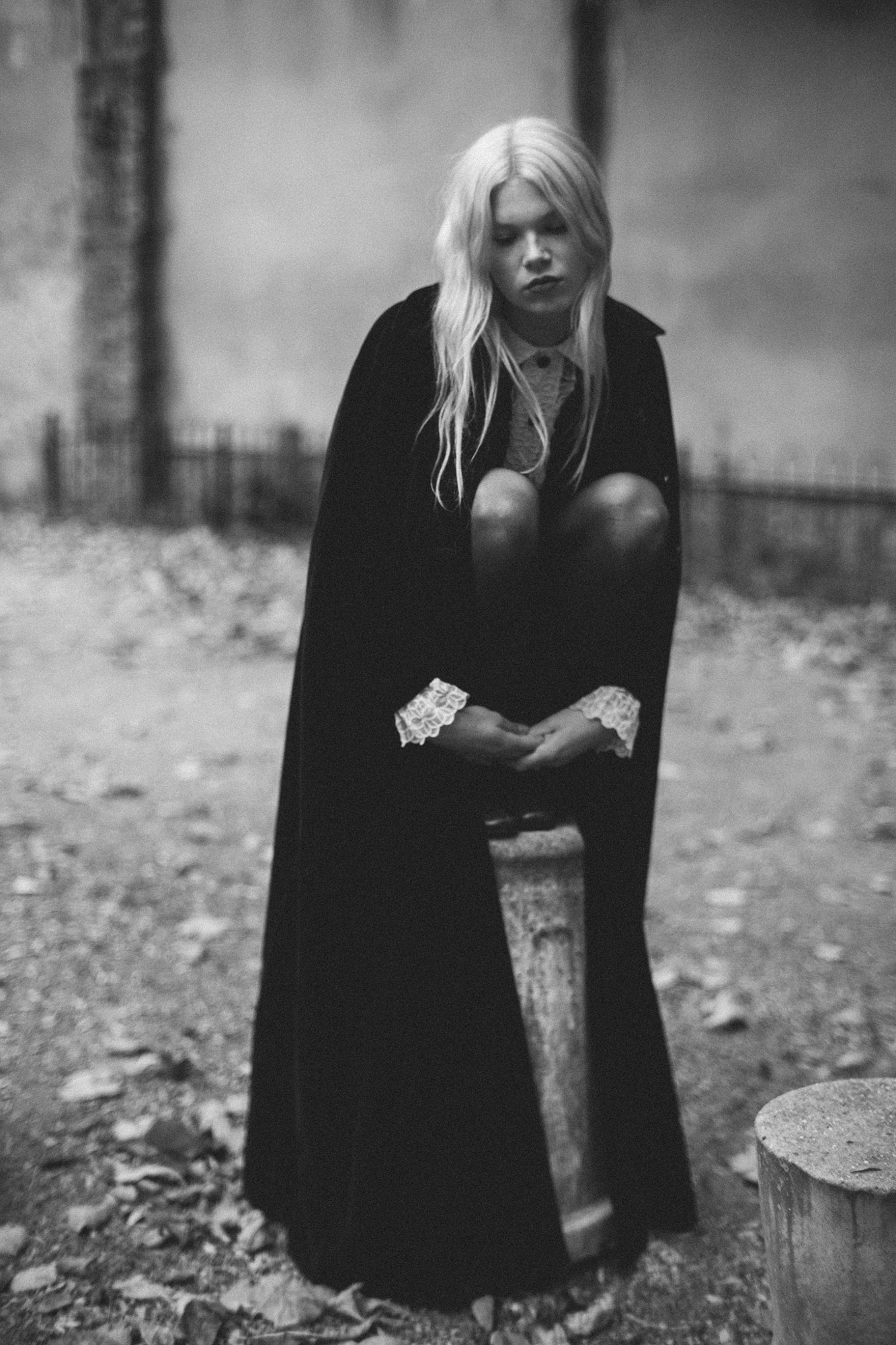 Atmospheric black and white portrait photography by Holger Nitschke showing a blonde woman in a dark cape with lace cuffs.
