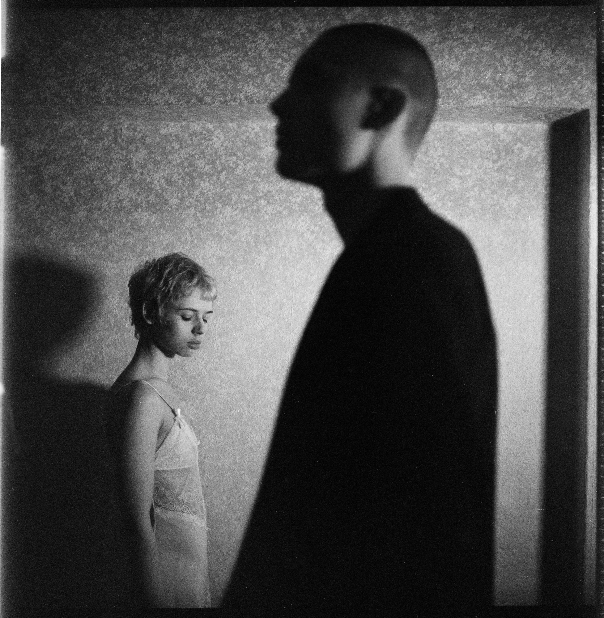 Cinematic black and white portrait by Holger Nitschke depicting a woman in a lace dress positioned behind a silhouetted profile.
