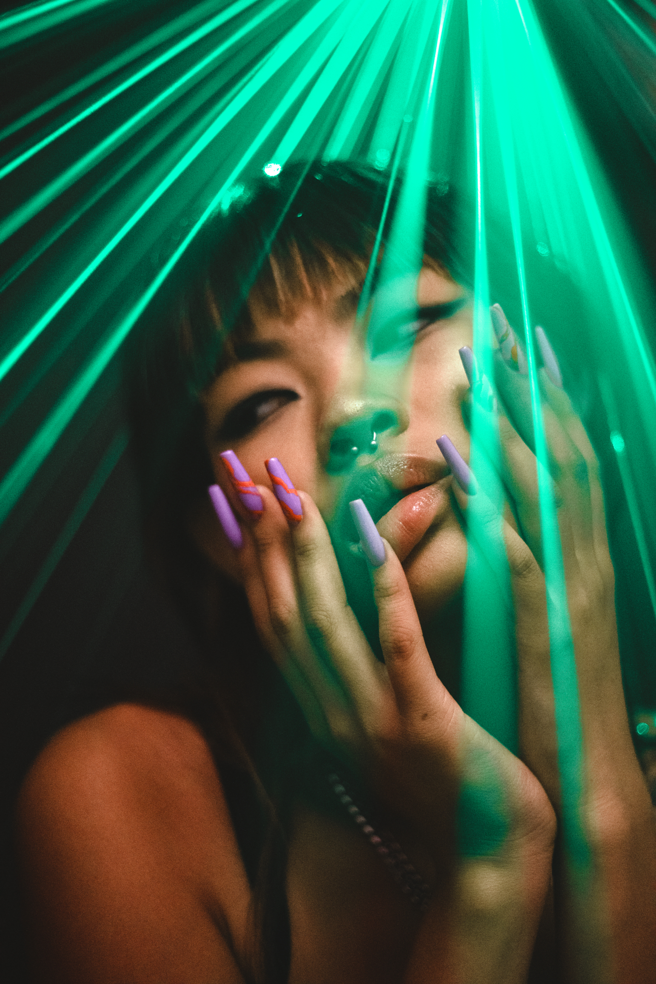 Experimental editorial portrait lighting by Micaela Belgiorno featuring vibrant green laser beams casting across a model's face.
