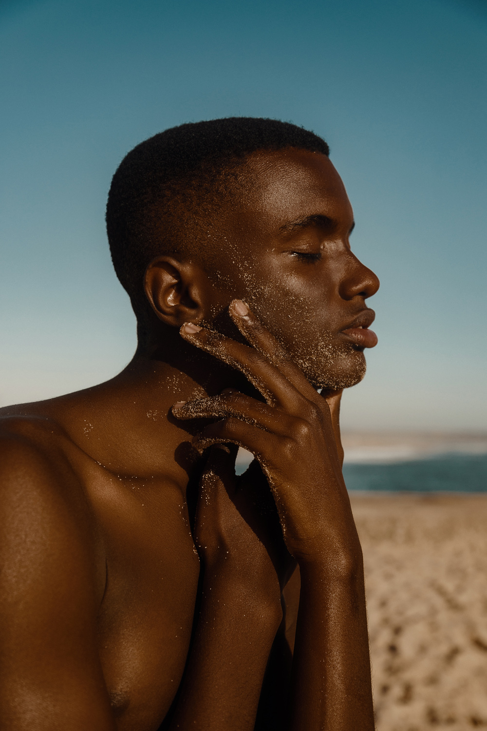 Close-up profile portrait of a man with sand on his skin, showcasing male beauty photography by David Velez.