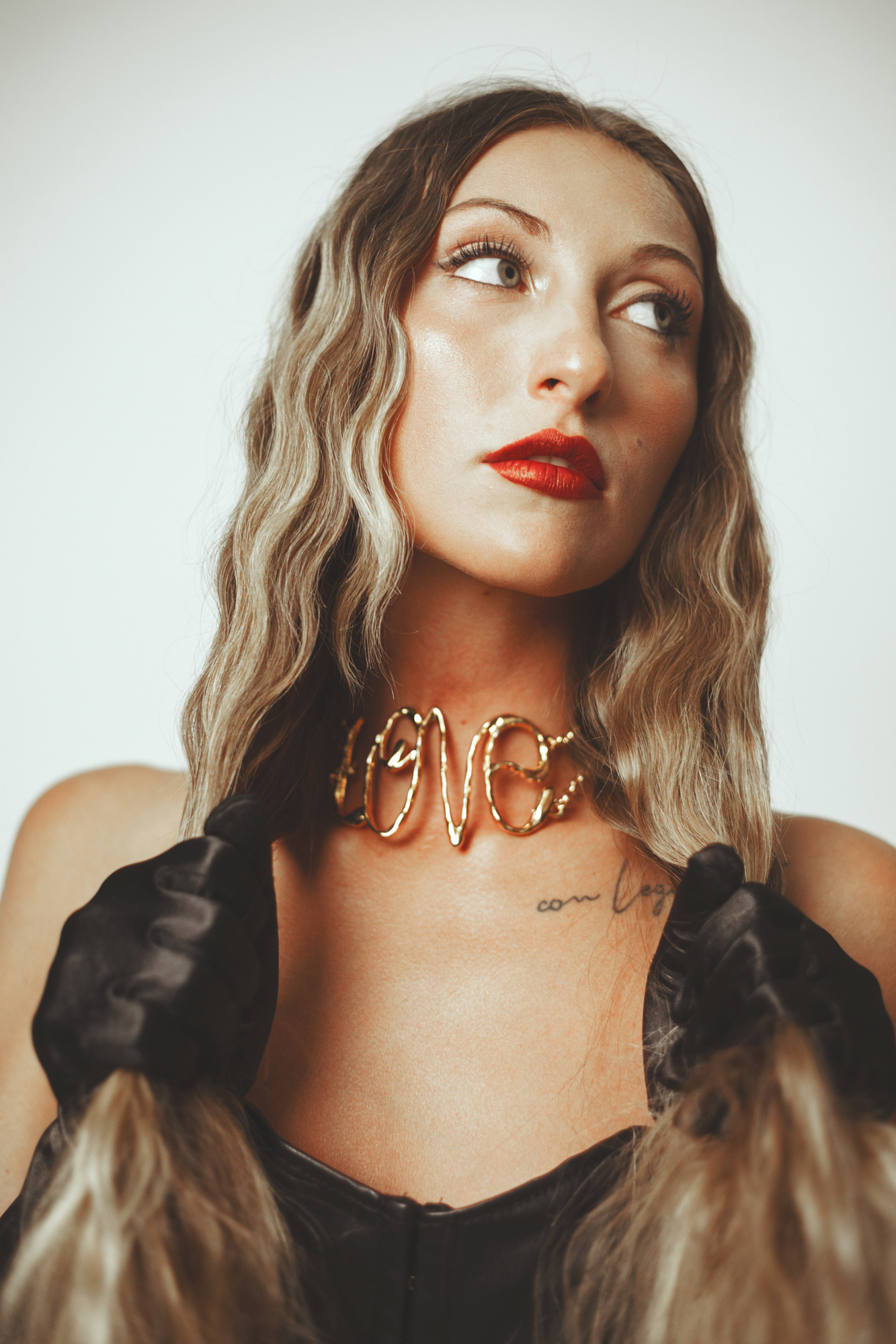 High-fashion editorial portrait displaying a metallic gold wire choker and black leather gloves under warm studio lights.