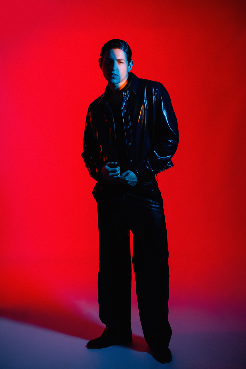 Studio fashion portrait of a man in leather under red and blue lights, styled by David Velez photography.