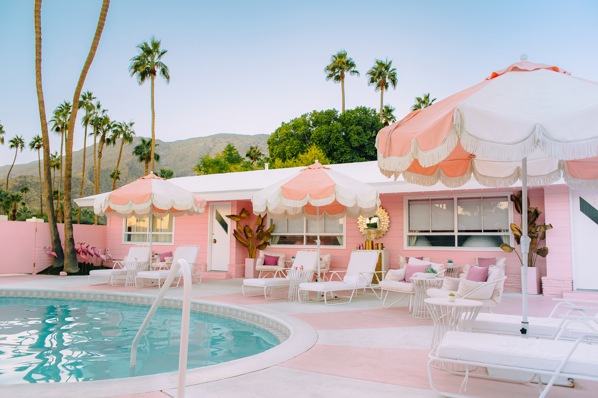 A retro pink motel poolside with white and pink umbrellas and lounge chairs, displaying a bright and vibrant color palette perfect for summer.